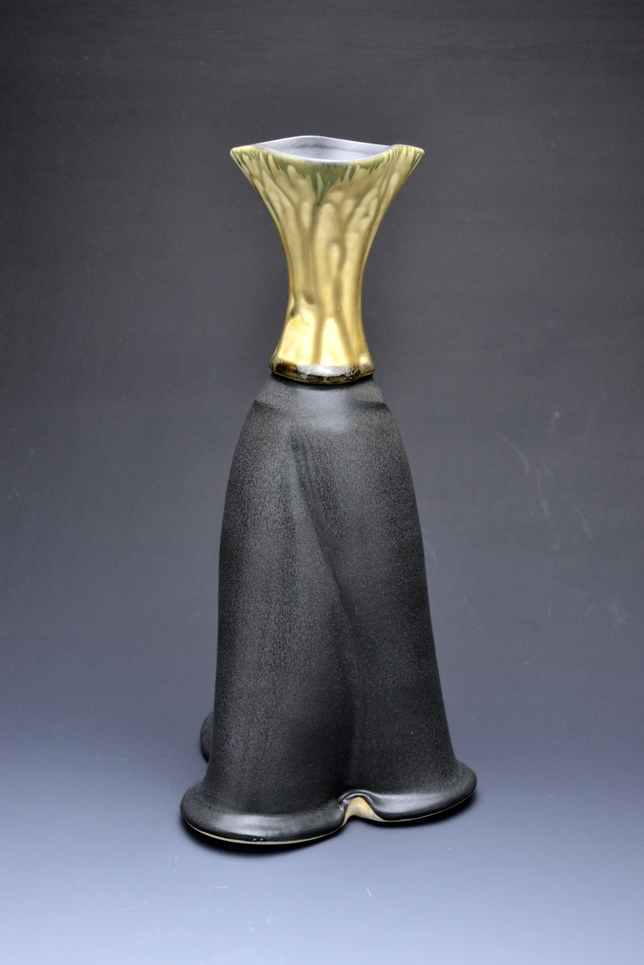 A ceramic vase with a black, textured, and flowing design, topped with a contrasting gold and green lip. By Conner Burns