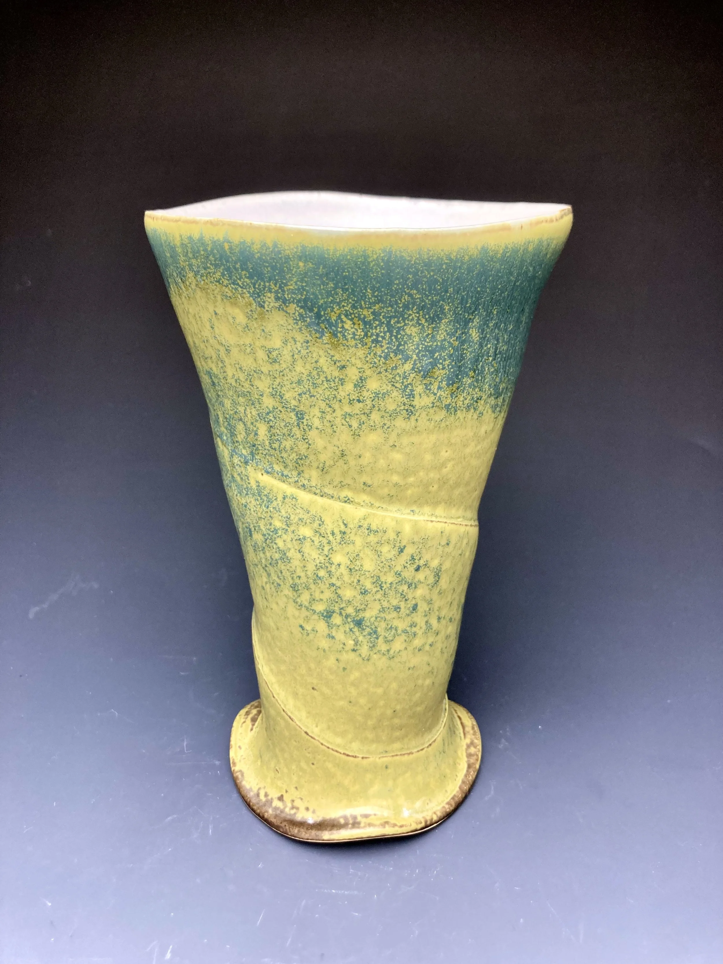 A ceramic vase with a yellow-green glaze, speckled with darker green, against a black background.   by Conner Burns