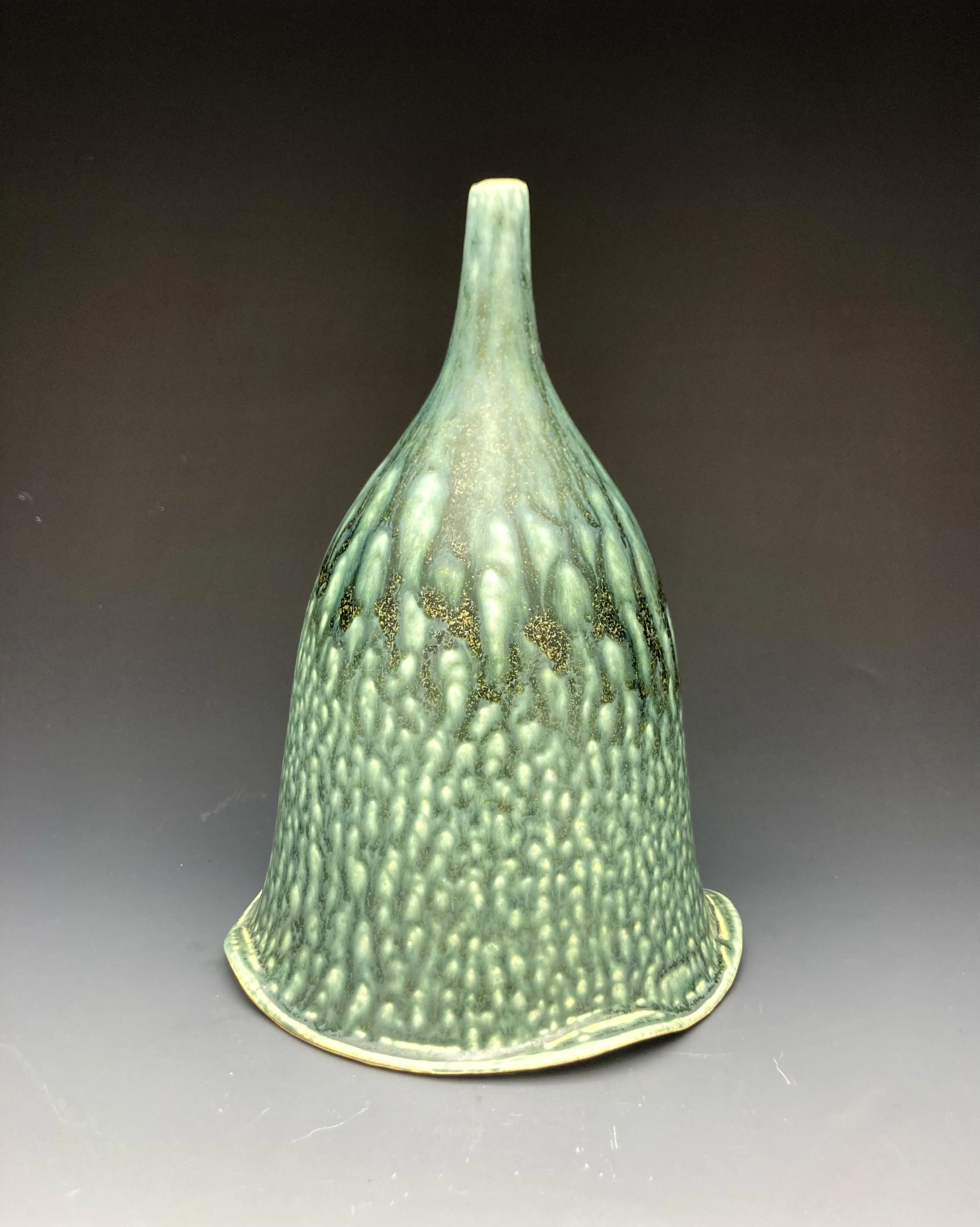 Green ceramic vase with textured surface and elongated neck on a dark background. By Conner Burns