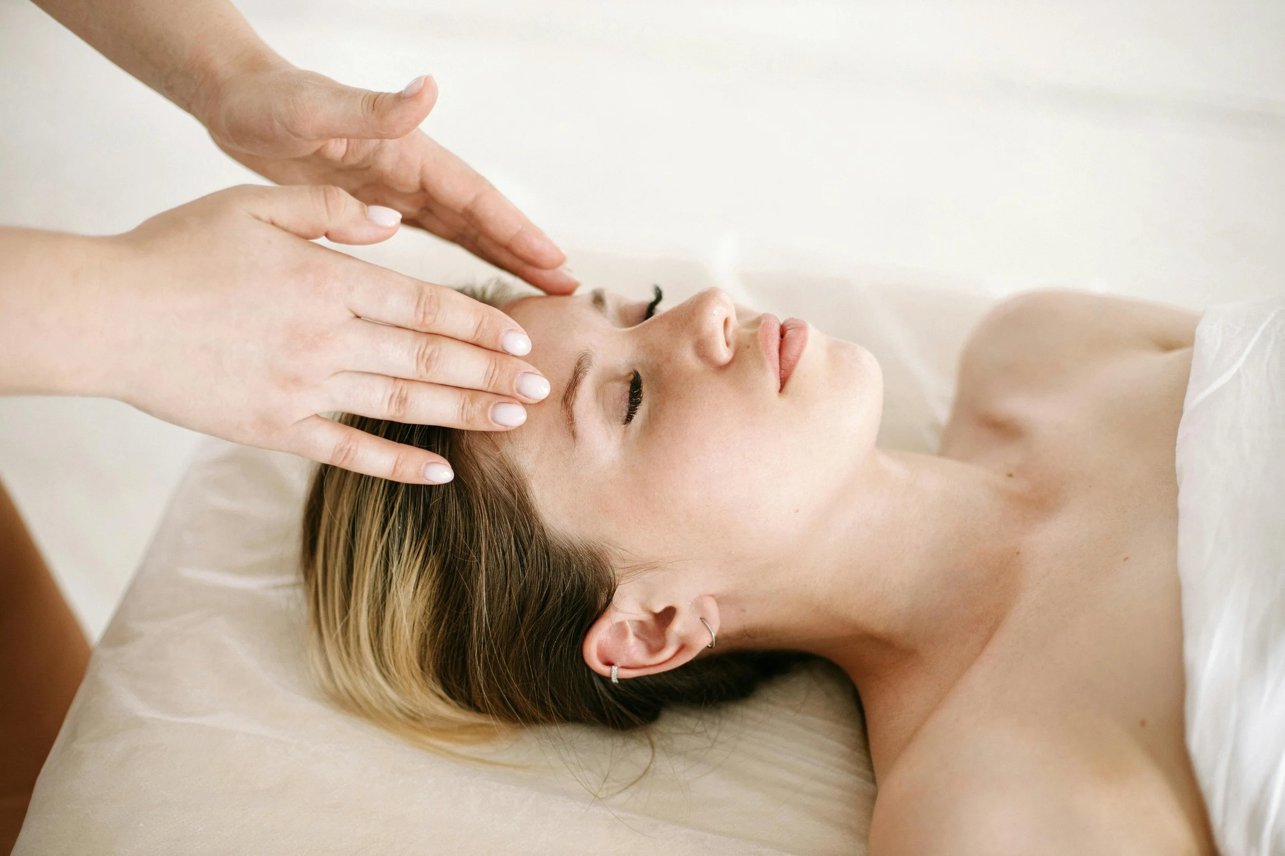 A woman lying on a bed receiving a head massage from a therapist.