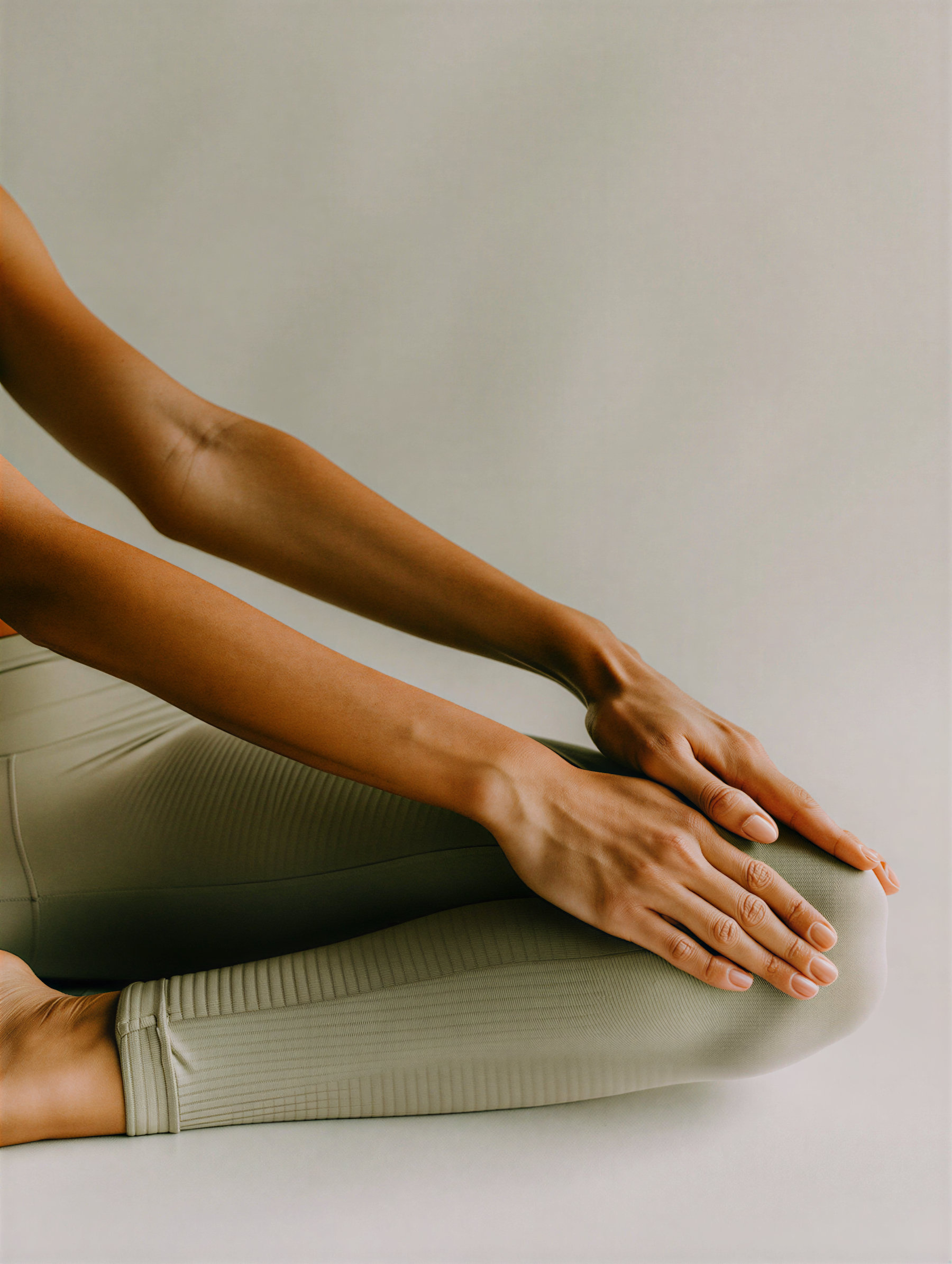 Close-up of a person in a stretching yoga pose, only the arms, hands, and part of the torso are visible, leaning forward on a cushioned surface with a plain background.