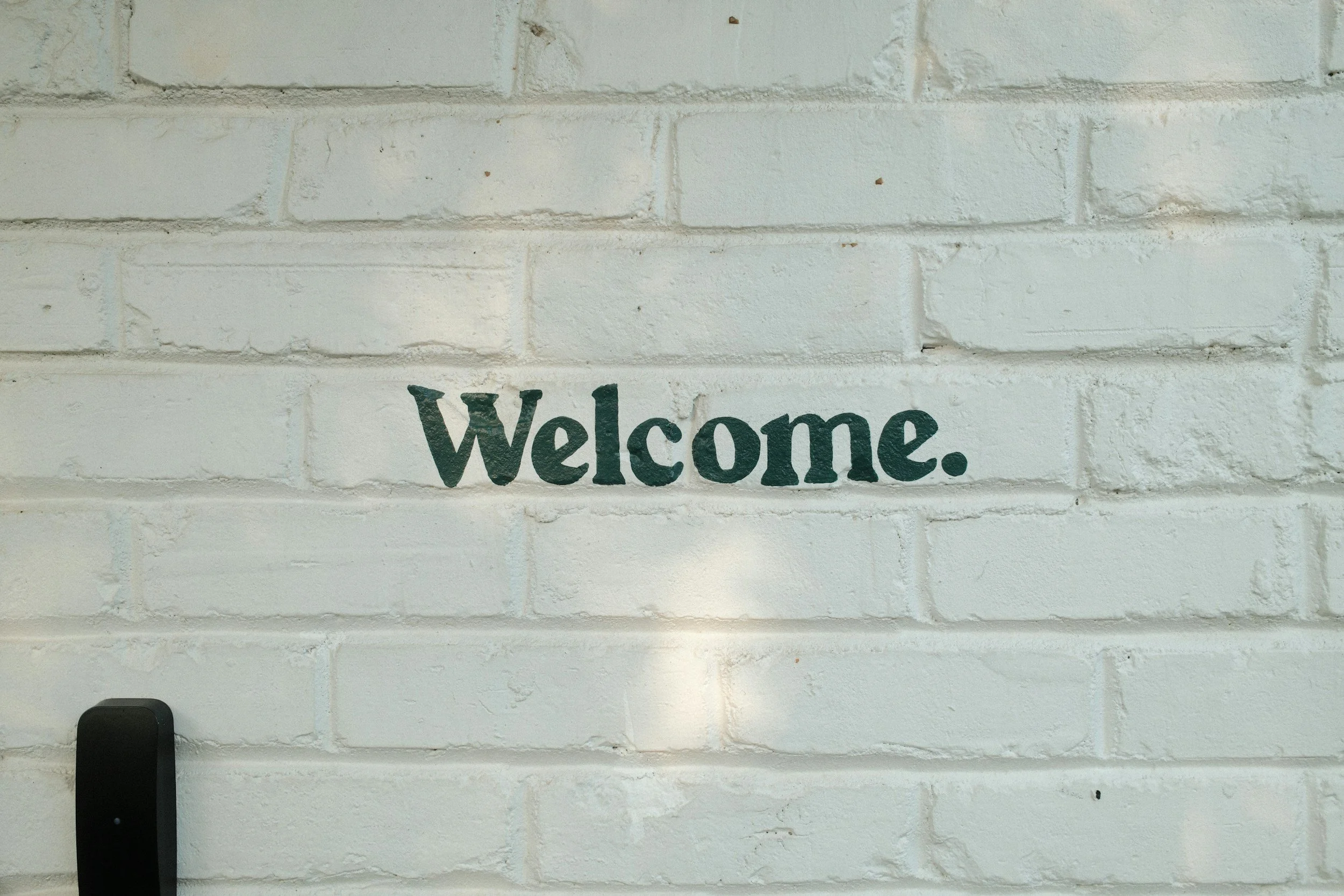 White brick wall with the word 'Welcome.' painted in dark green.