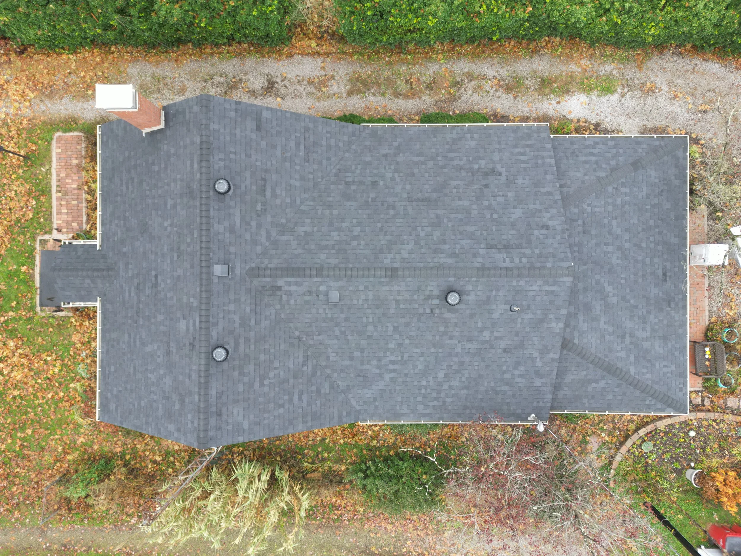 Overhead view of a house with a dark gray shingle roof, surrounded by a yard with fallen leaves and plants.