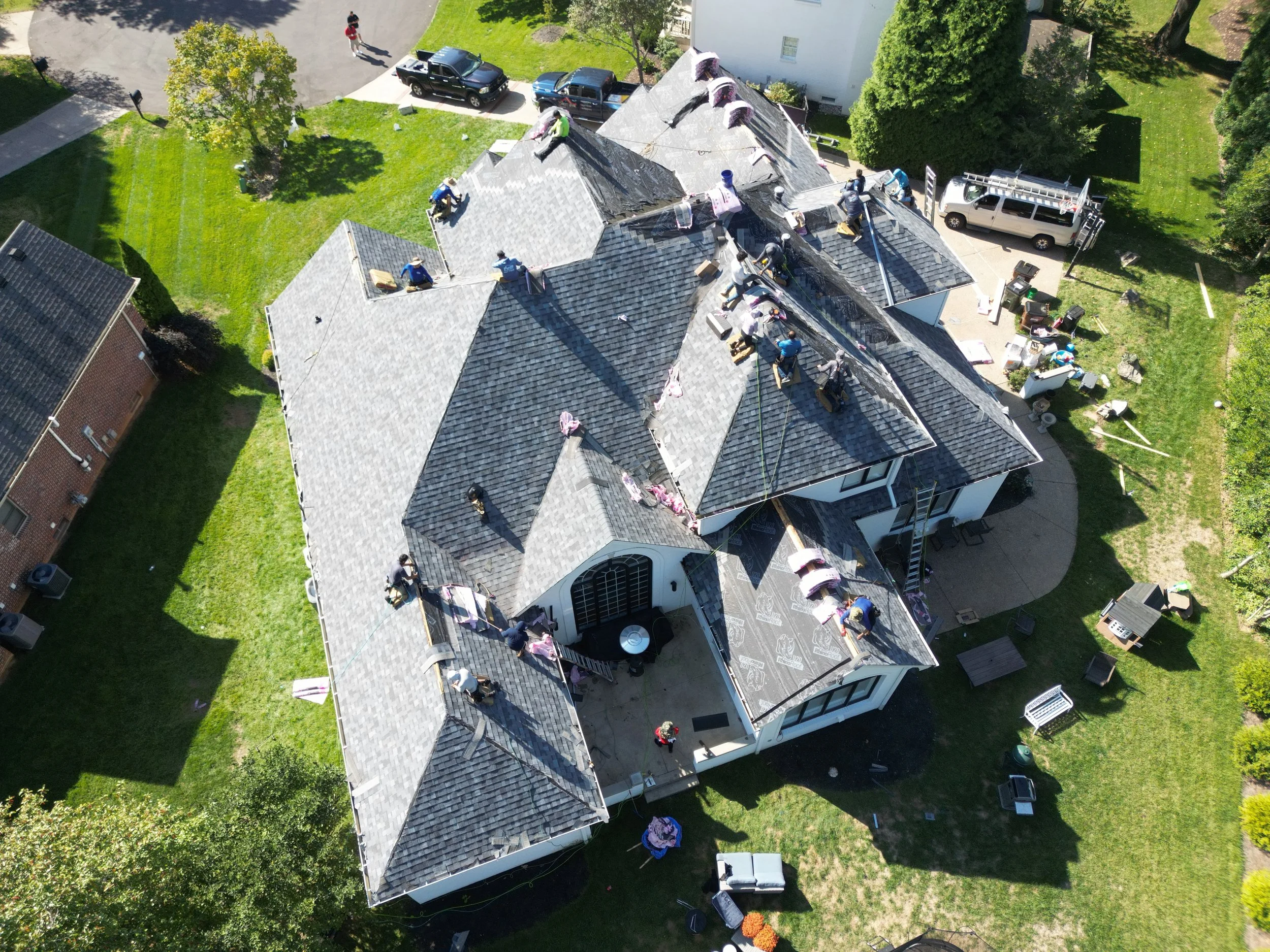 Aerial view of a house roof with multiple workers installing or repairing shingles on the roof.