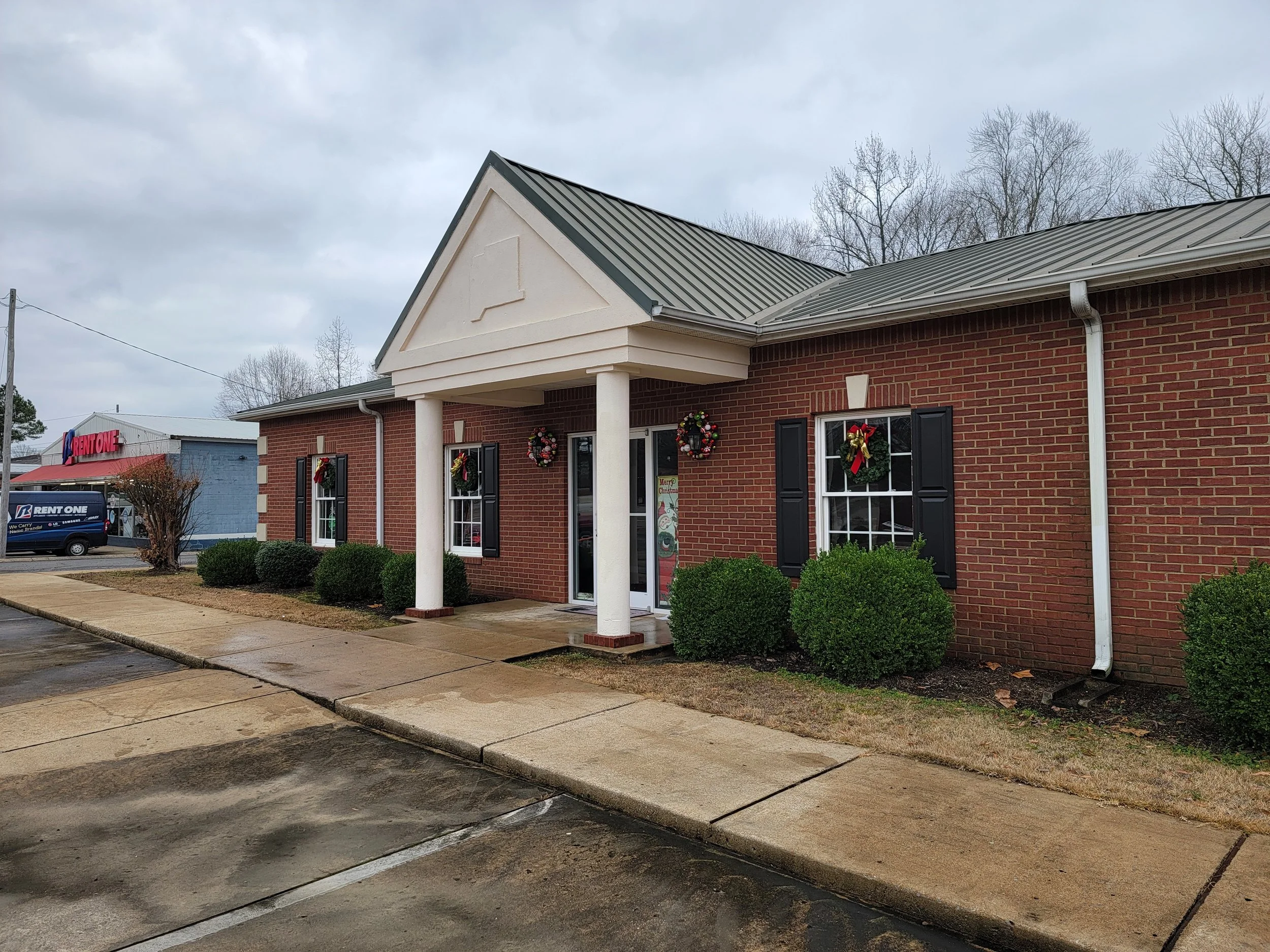 Brick building decorated with Christmas wreaths and bows amidst a cloudy sky.
