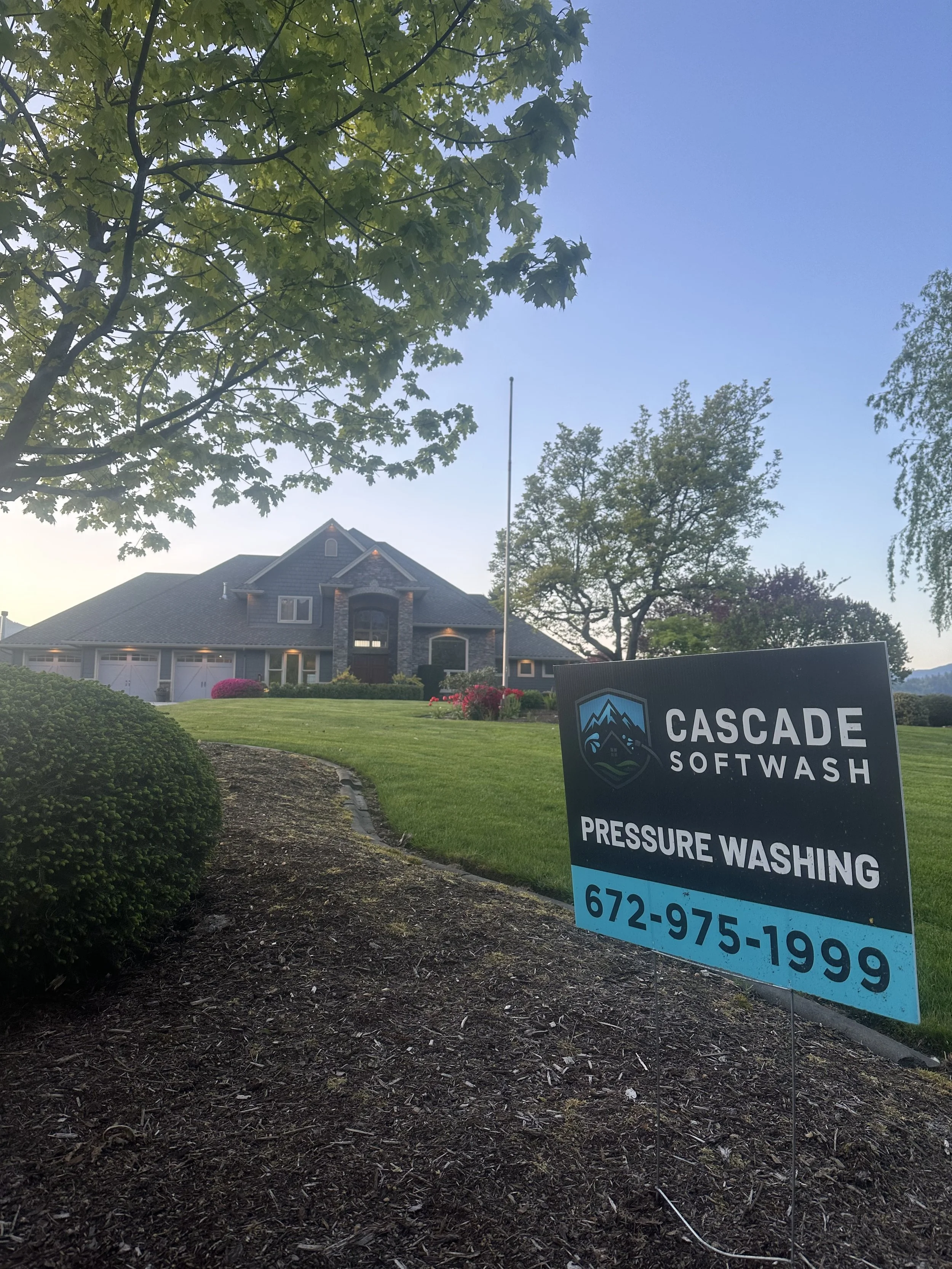 Residential house with a well-maintained lawn and garden, trees surrounding the property, and a sign for Cascade Softwash indicating pressure washing services.