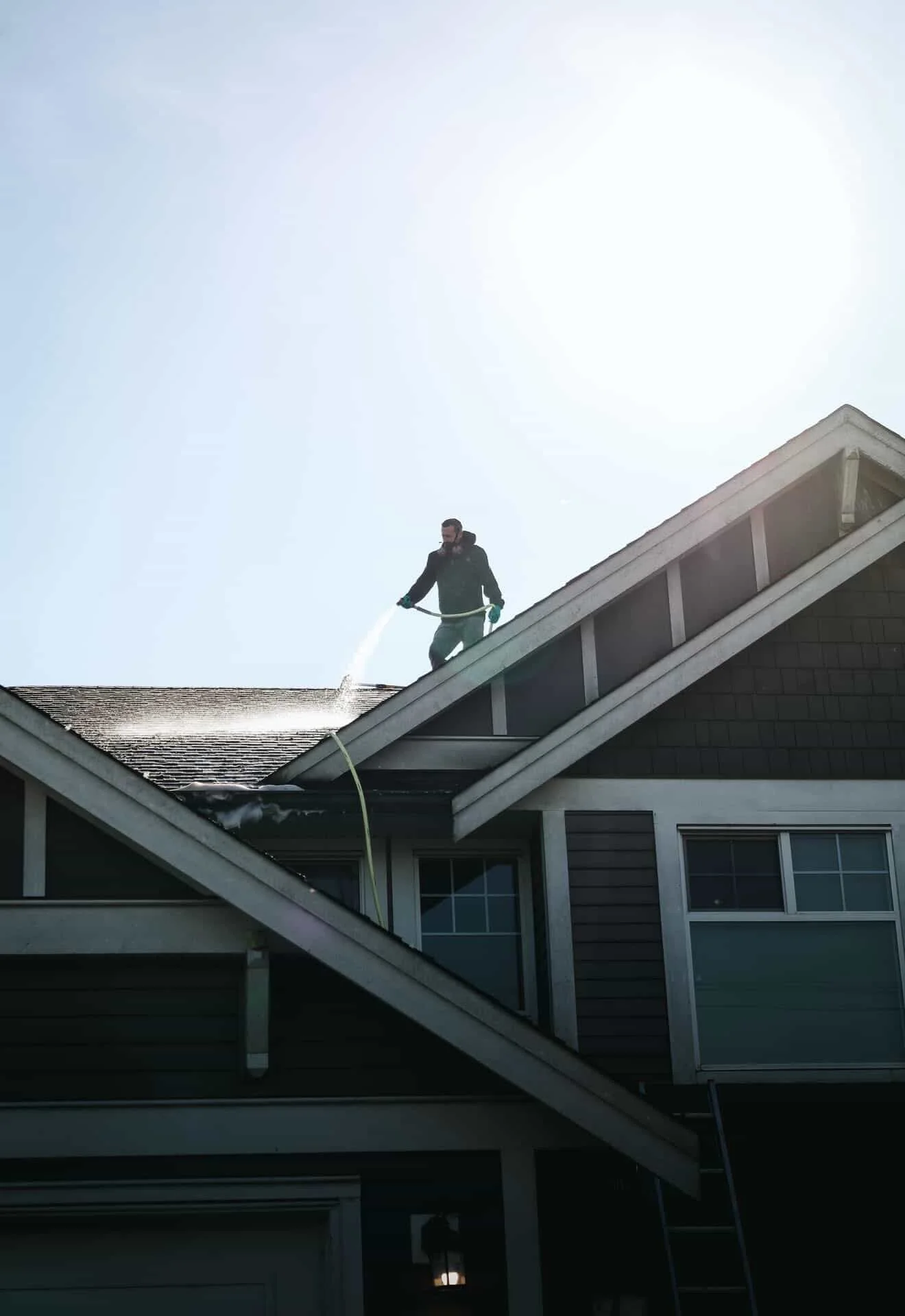 A person cleaning the roof of a house with a hose under bright sunlight.