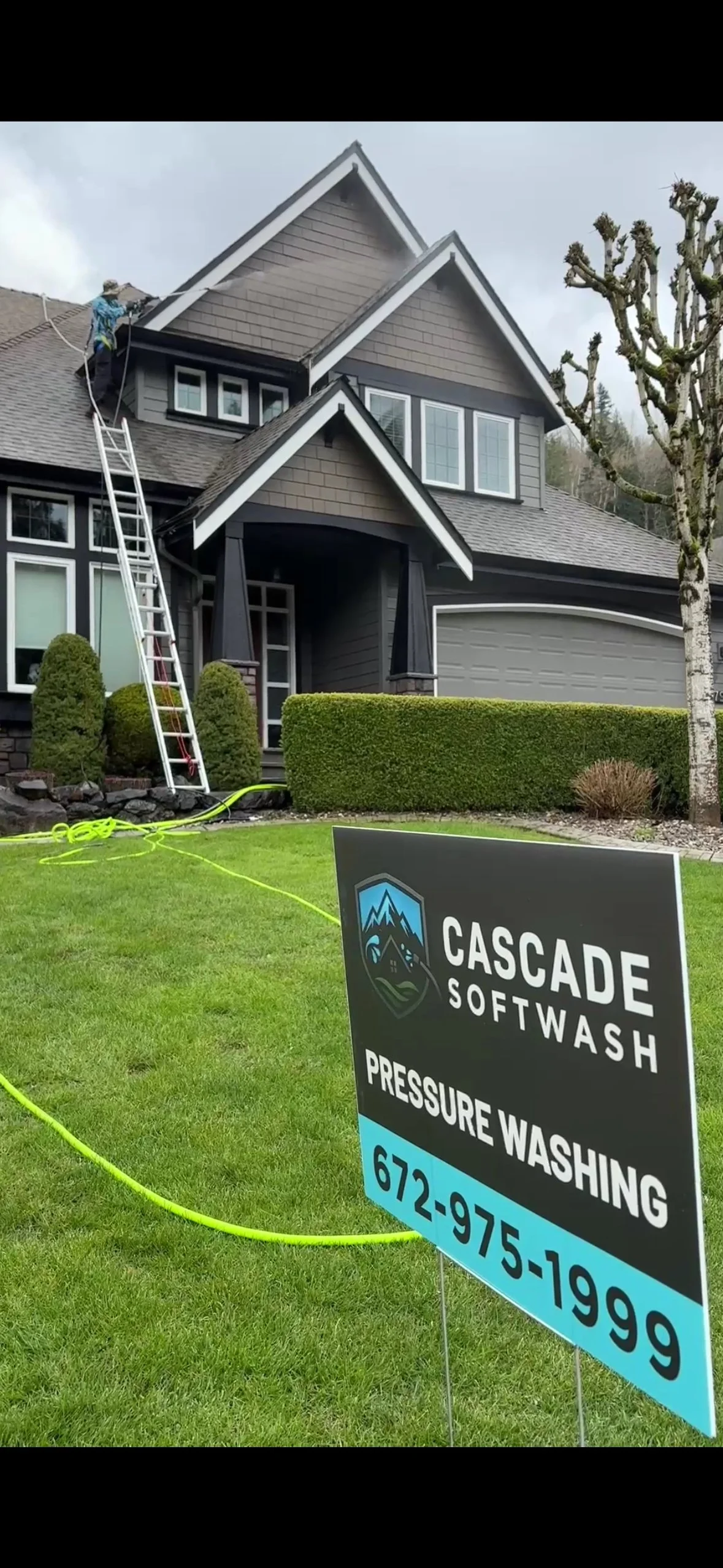 A house being pressure washed by a worker on a ladder, with a Crest Cascade SoftWash sign in the front yard.