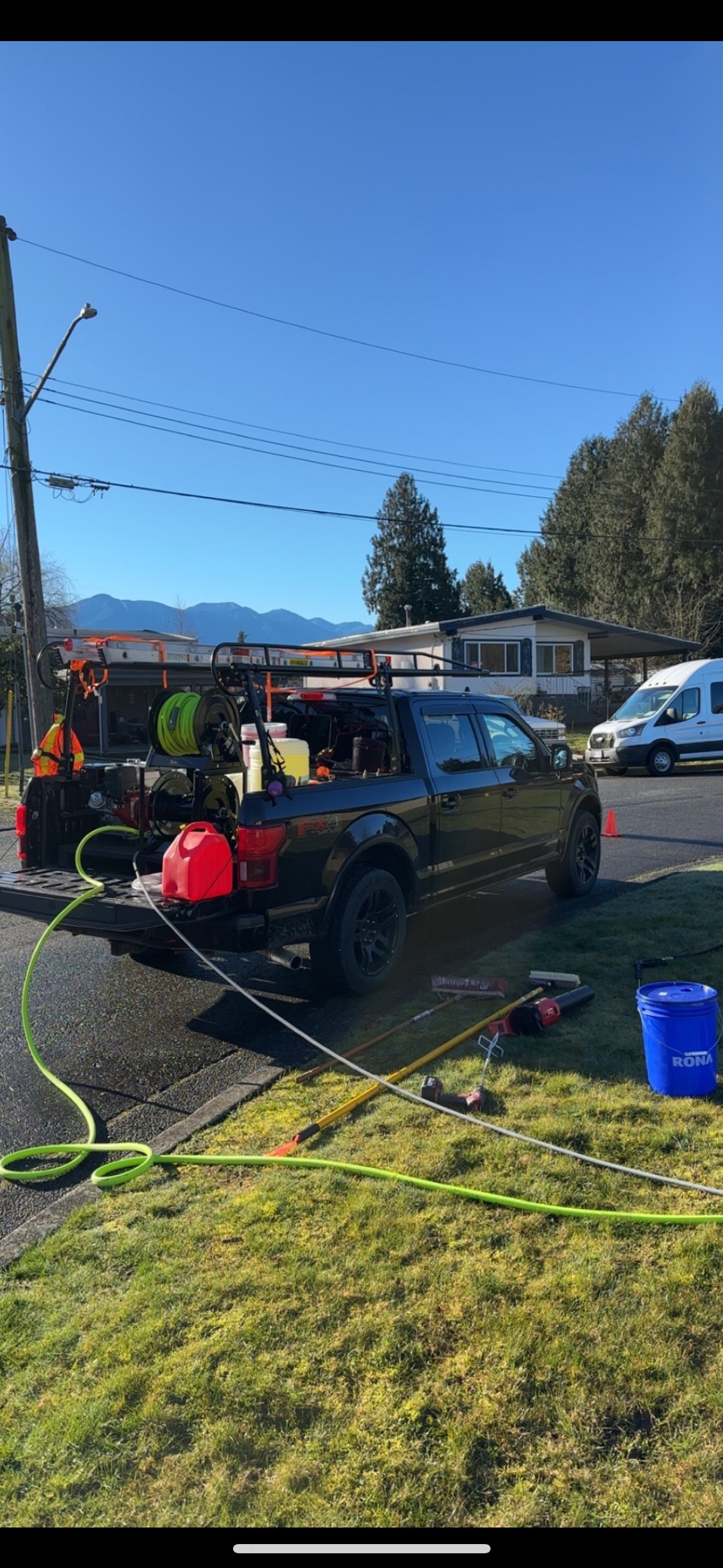 Utility work truck parked on the side of a residential street with tools, hoses, and equipment in the truck bed, and fireman tools on the ground nearby under a clear blue sky.