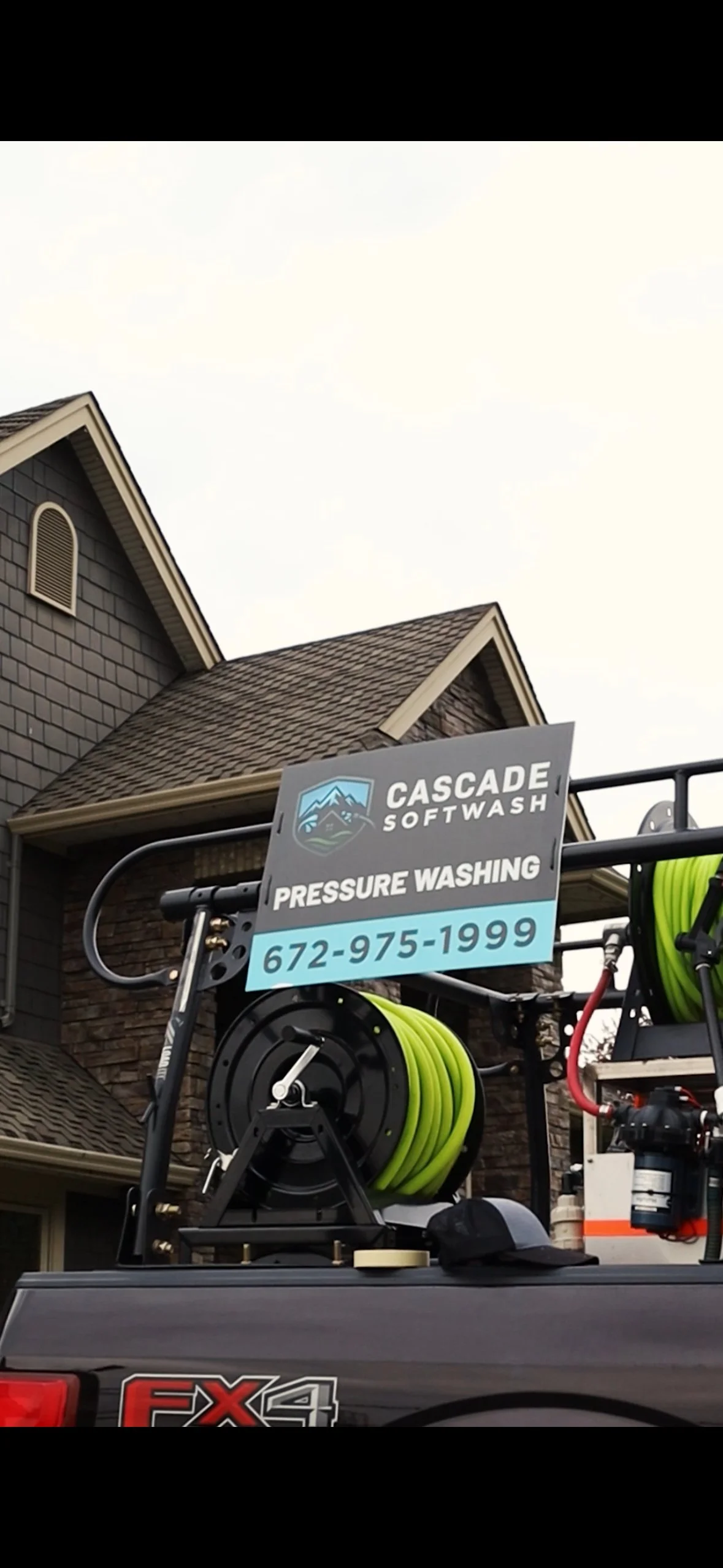A sign for Cascade SoftWash pressure washing company mounted on a service vehicle, with a house in the background.