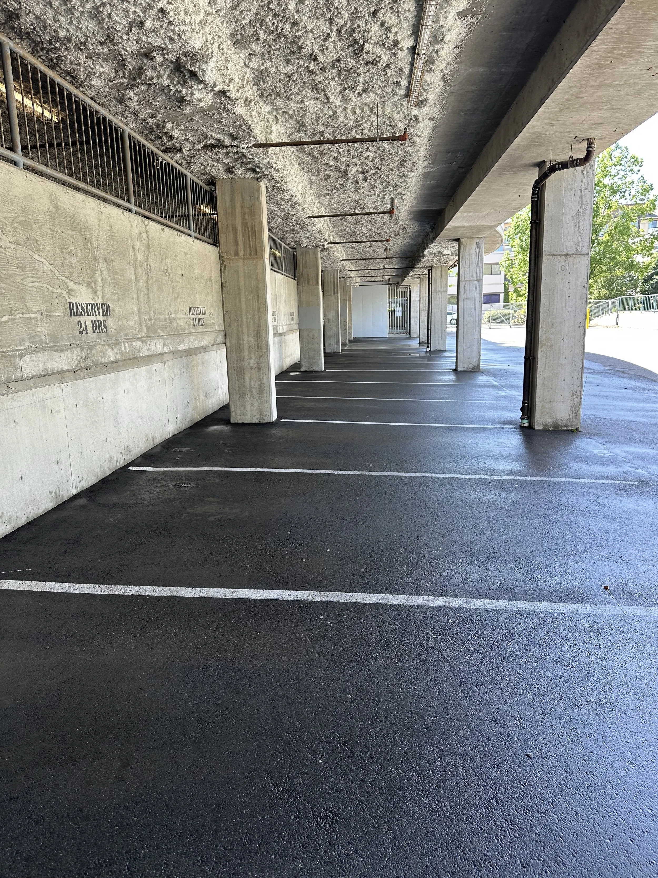 Underground parking garage with concrete walls, pillars, and designated parking spots marked by white lines, some spots reserved.