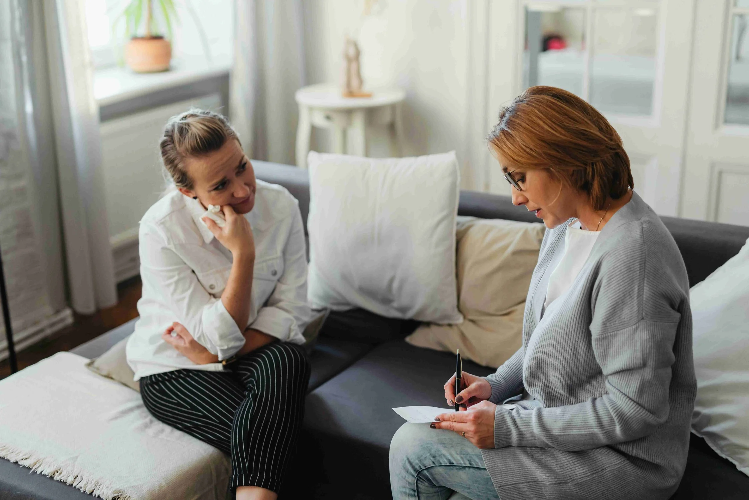 A woman talking to a young girl sitting on a couch, with the woman writing notes on a notepad.