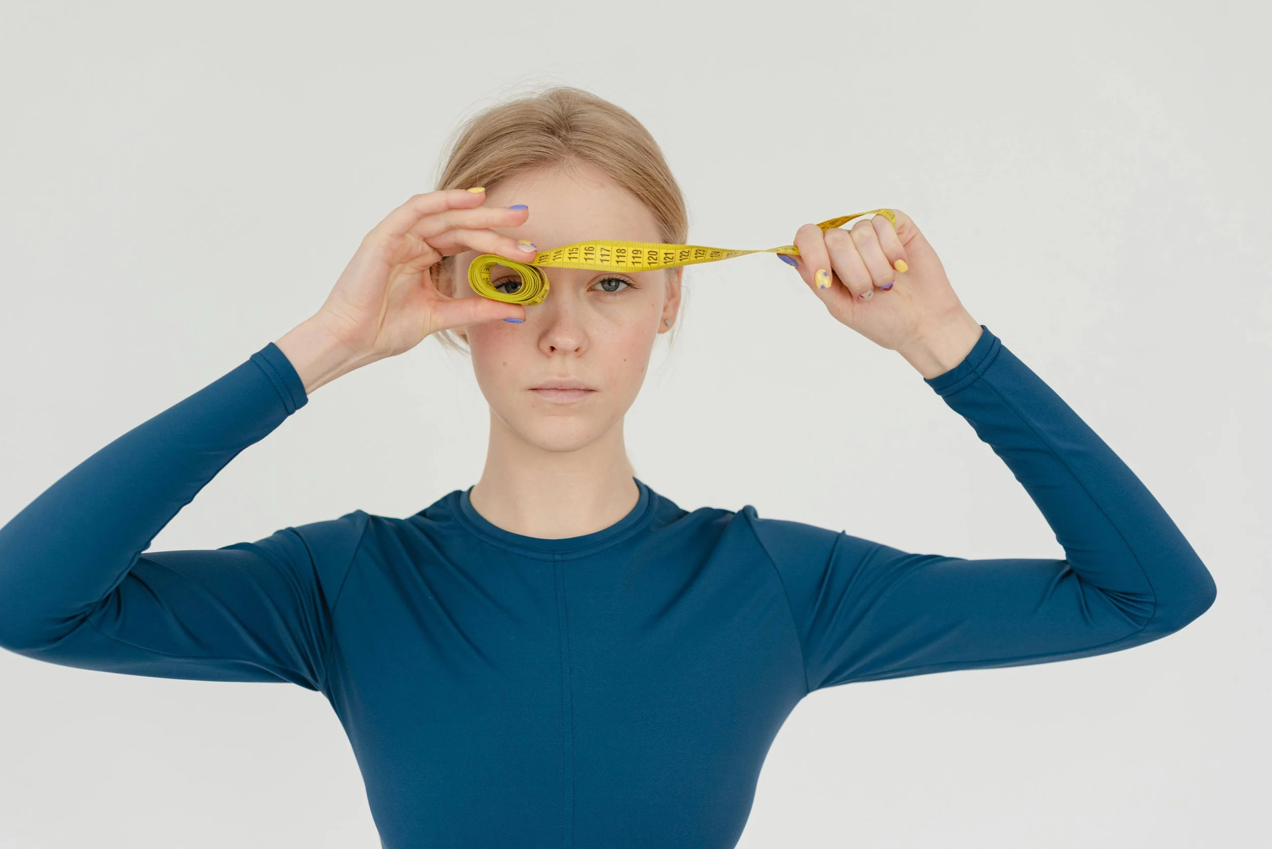 A woman measuring her head with a yellow measuring tape against a plain white background.