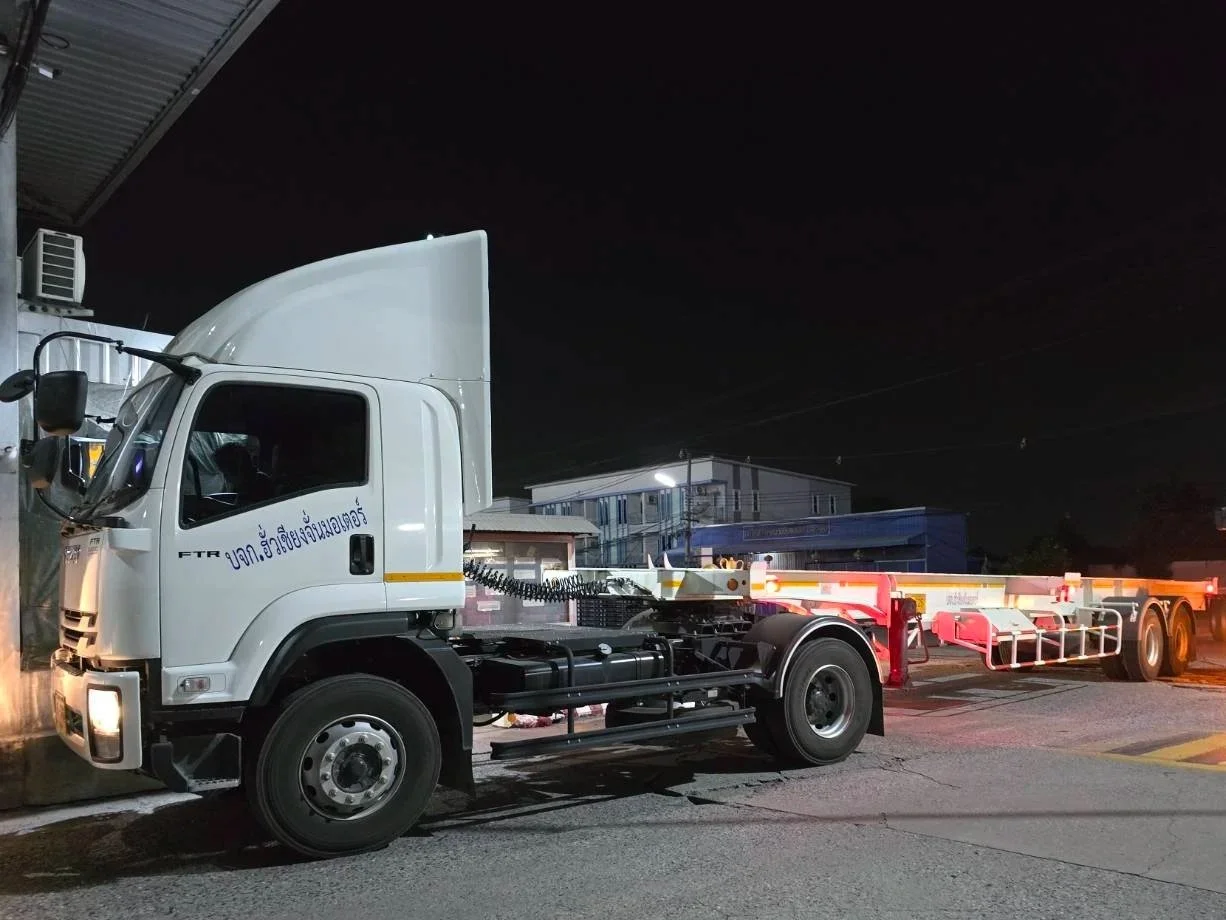 White flatbed tow truck parked on a street at night, with buildings in the background.