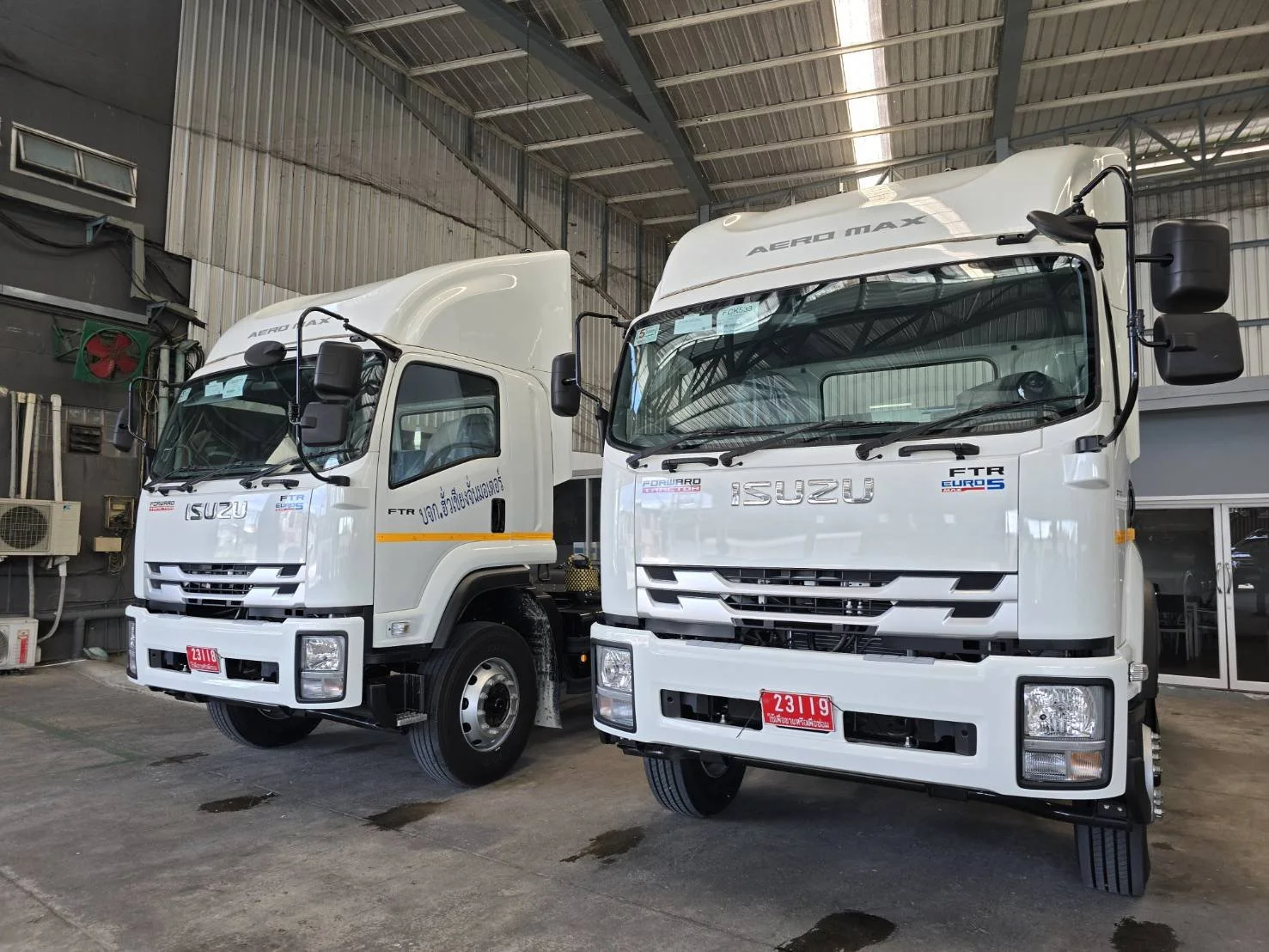 Two white Isuzu trucks parked inside a garage or warehouse.