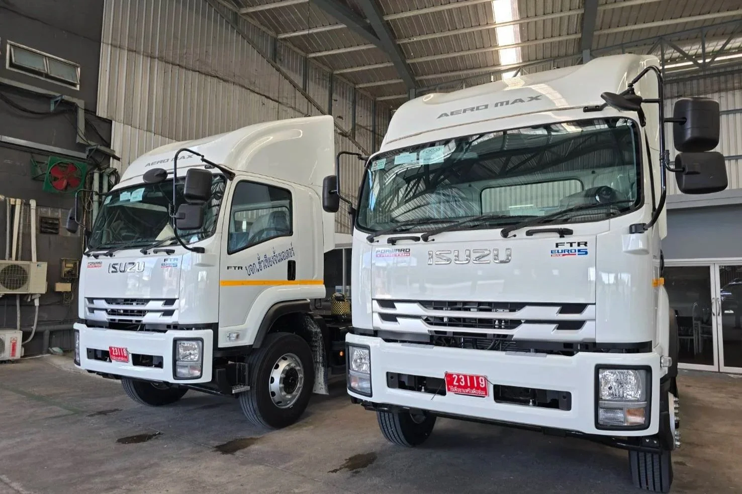 Two white Isuzu trucks parked inside a warehouse.