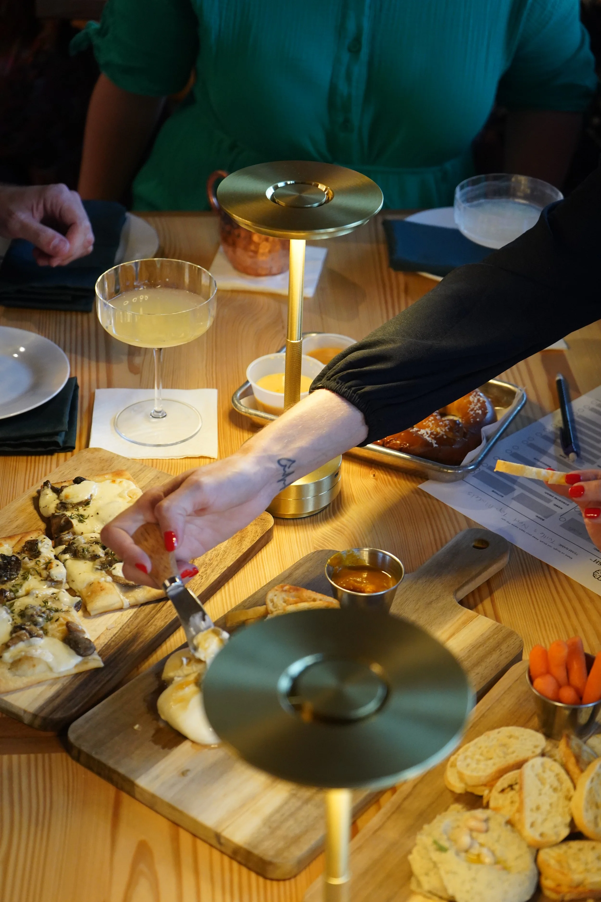 People enjoying appetizers at a restaurant, with pizza, bread, carrots, and drinks on the table.