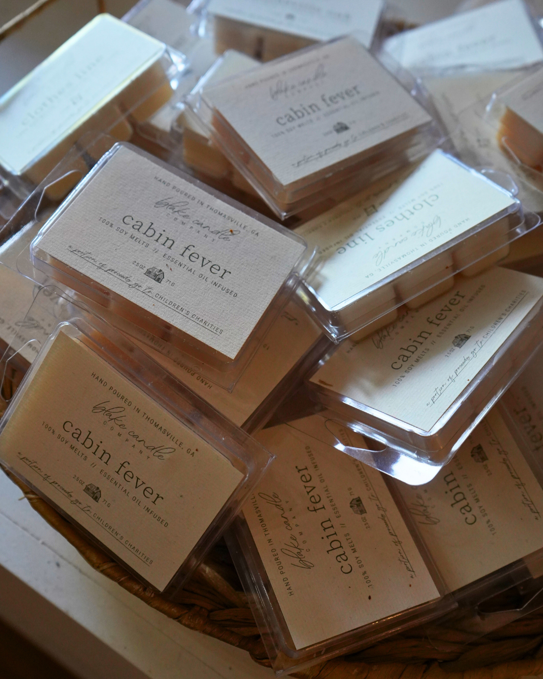 Several clear plastic containers with beige labels reading "cabin fever" scented candles in a basket.