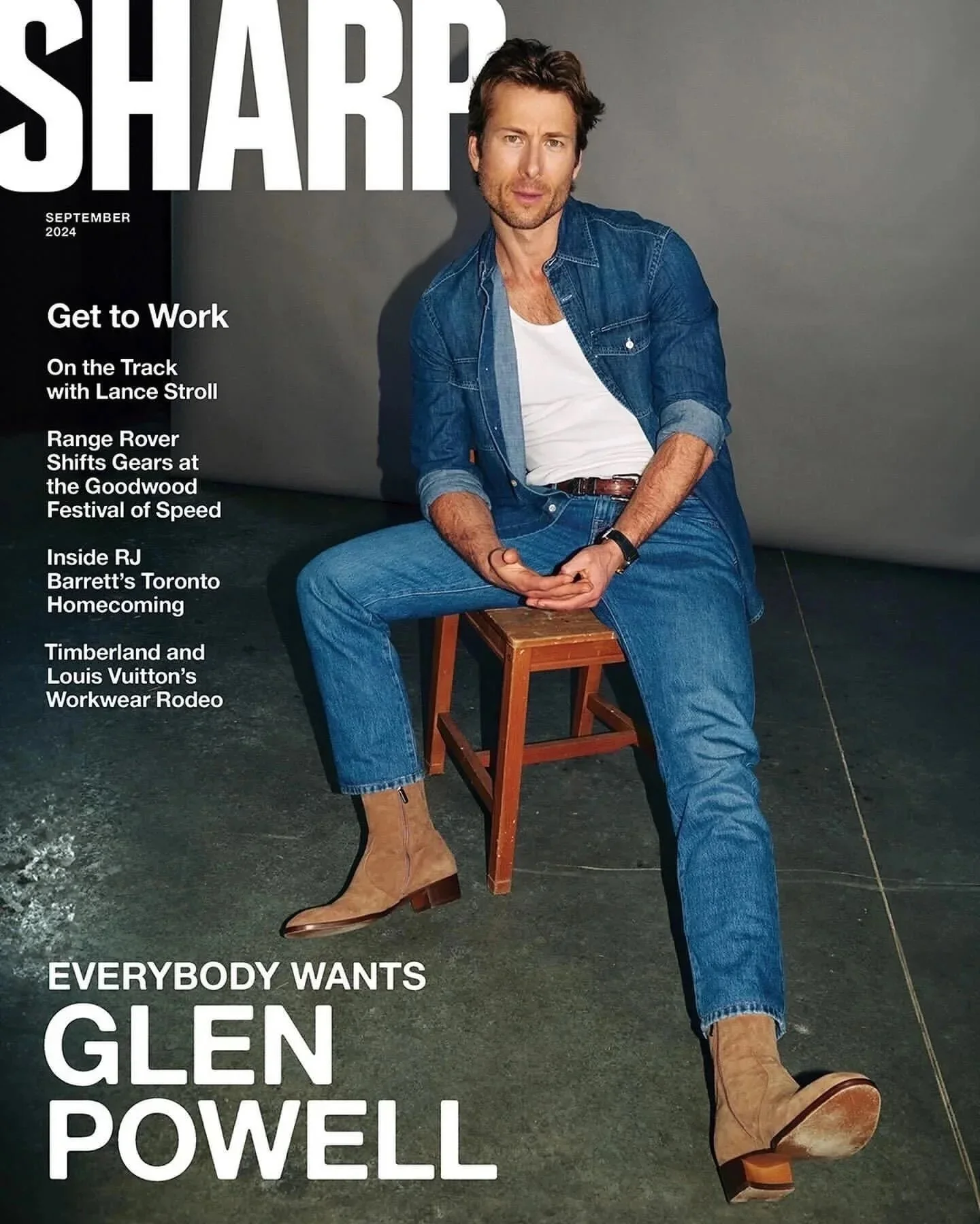 Magazine cover featuring Glenn Powell sitting on a small wooden chair against a plain wall, wearing a denim jacket, white t-shirt, jeans, and tan boots, with magazine headlines on the left side.