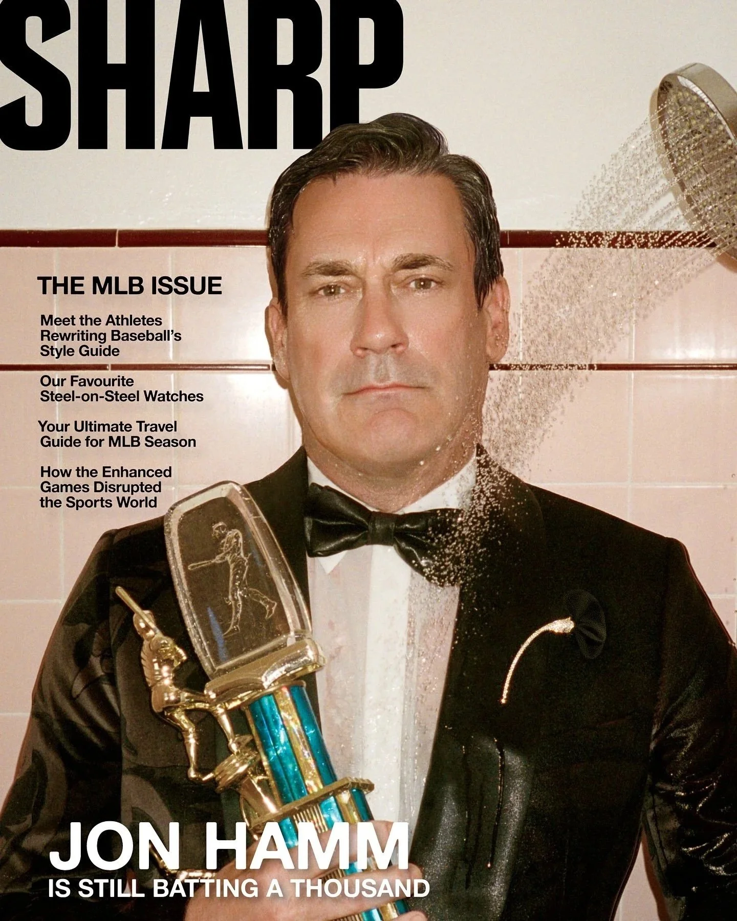 Jon Hamm poses for a magazine cover in a locker room shower. He is holding a vintage sports trophy and wearing a tuxedo with a Tiffany & Co. brooch.