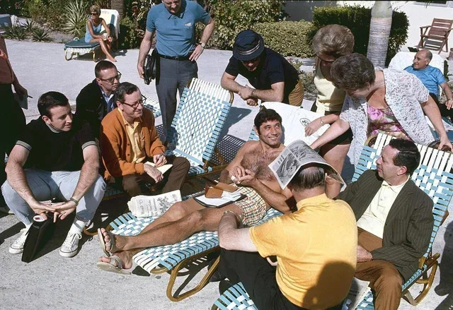 Quarterback Joe Naimath sits poolside surrounded by fans.