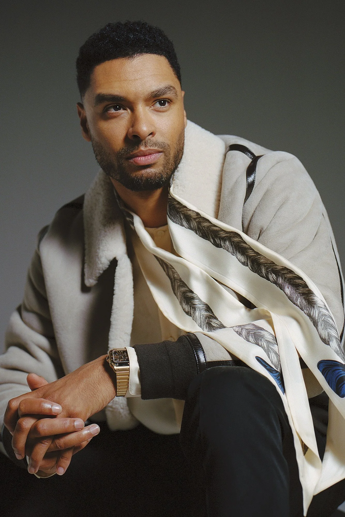 Rege-Jean Page wears a silk scarf while sitting for a fashion photoshoot
