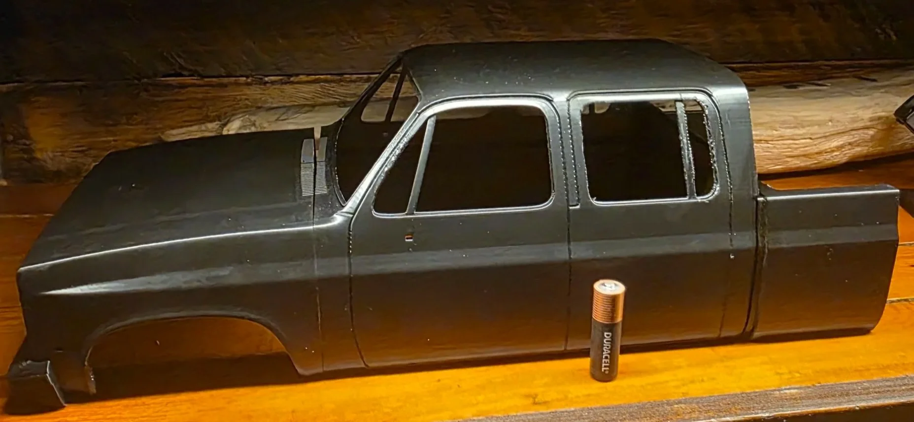 3D Unassembled black model car body on a wooden surface with a AA battery for scale.