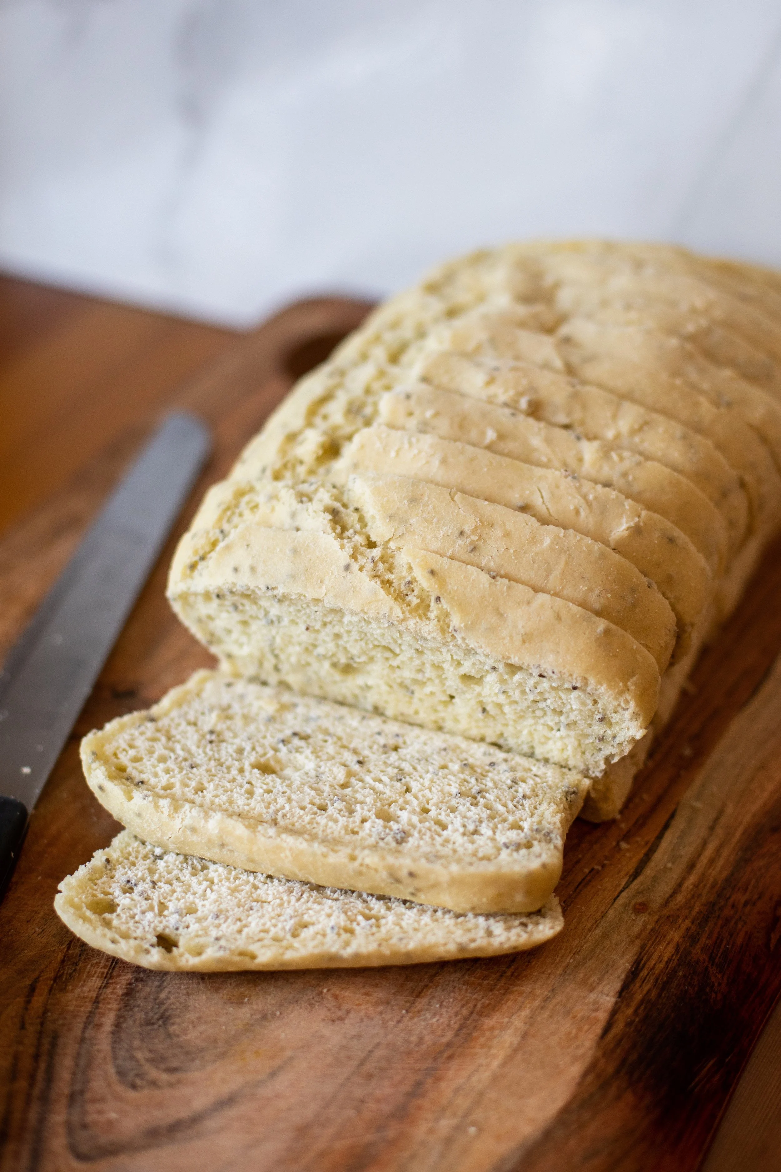 A sliced loaf of bread on a wooden cutting board with a bread knife beside it.