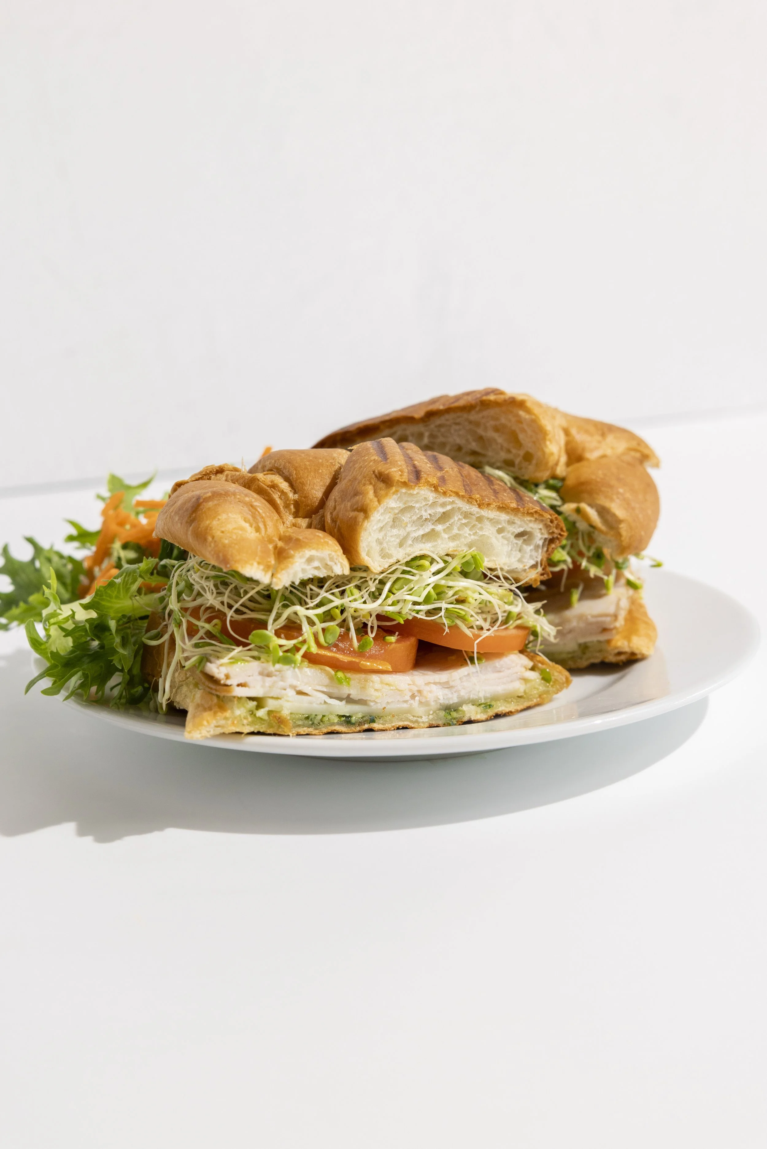 Close-up of a croissant sandwich filled with turkey, tomato, sprouts, lettuce, and green sauce.