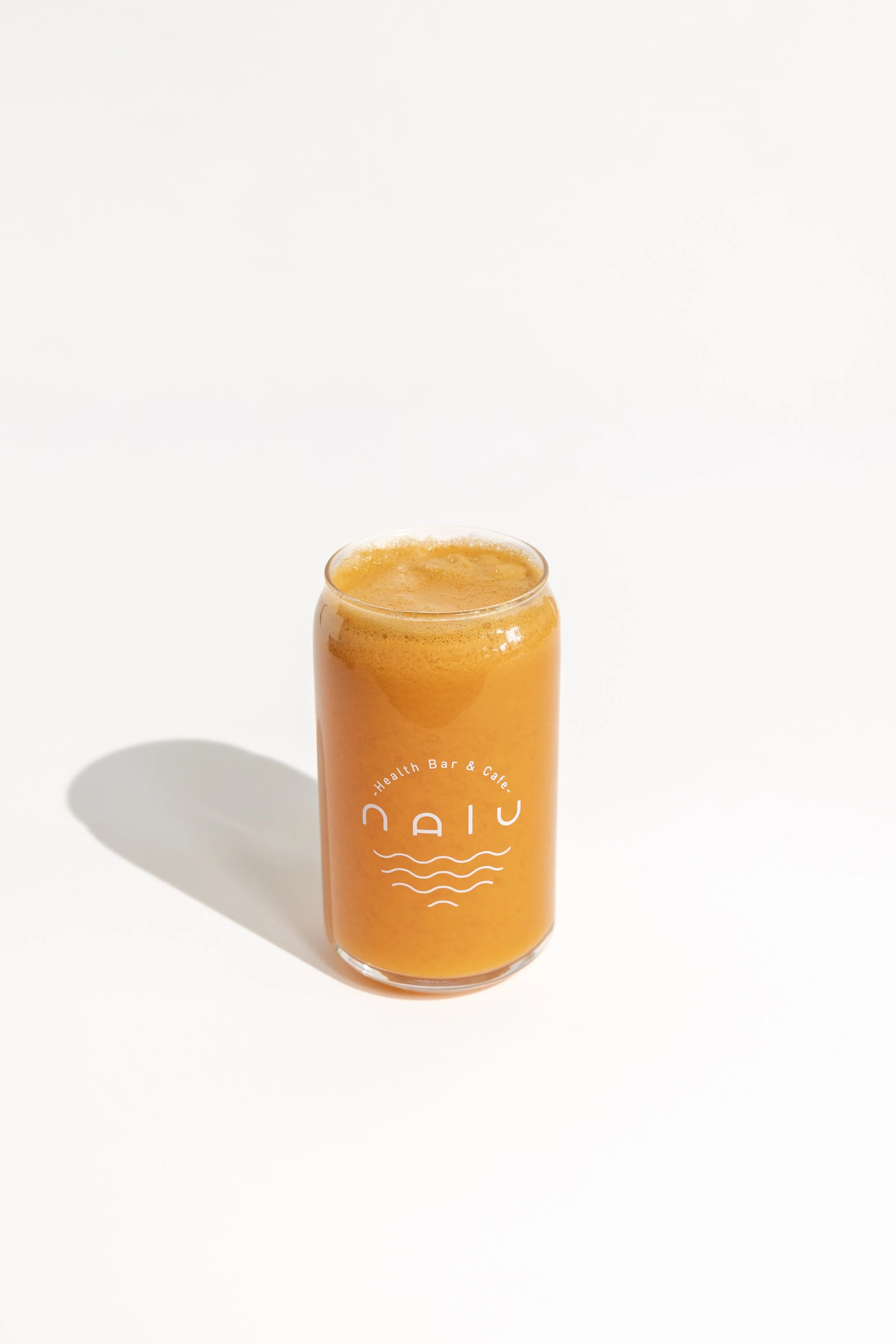 Two women holding colorful smoothies, one green and one red, in clear plastic cups at a gathering with food on the table.