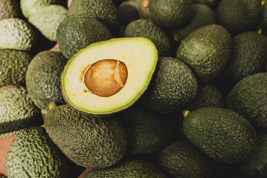 A group of ripe avocados, with one sliced open to reveal the seed inside.