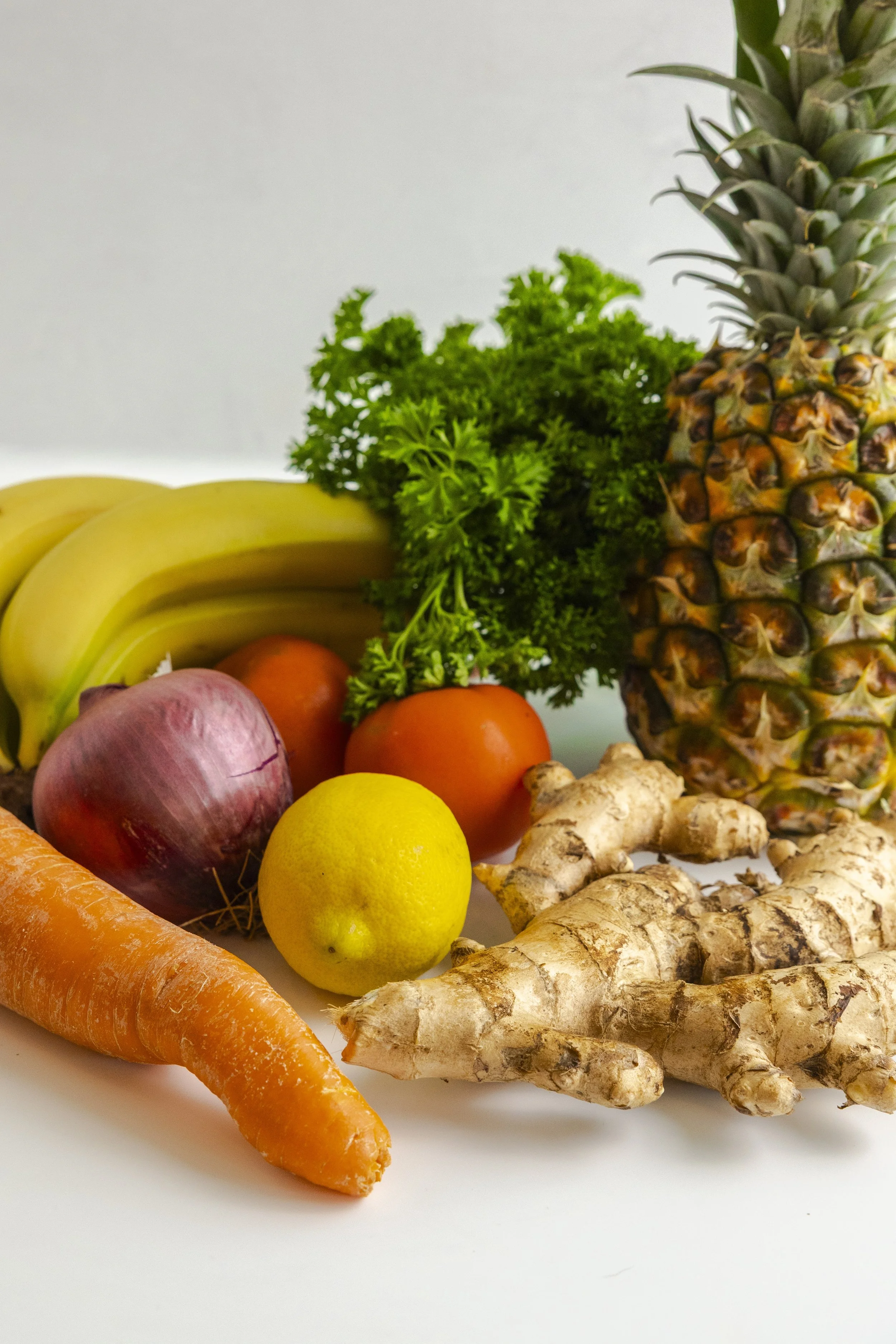 Fresh basil, heirloom tomatoes, and zucchini on a white cloth draped over a wooden surface, with a wicker basket containing more basil leaves placed on a wooden chair.