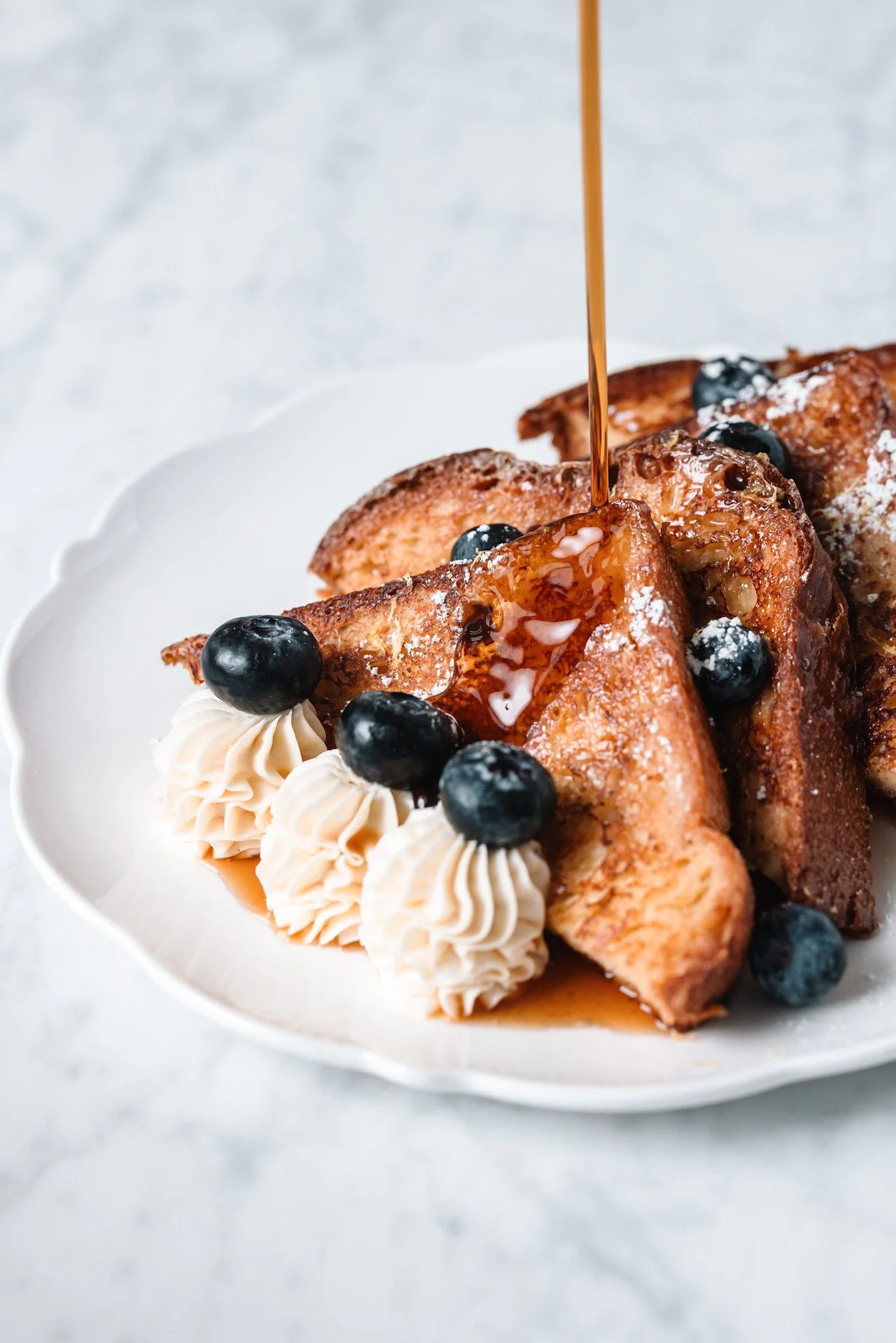 French toast with blueberries, whipped cream, and syrup on a white plate.