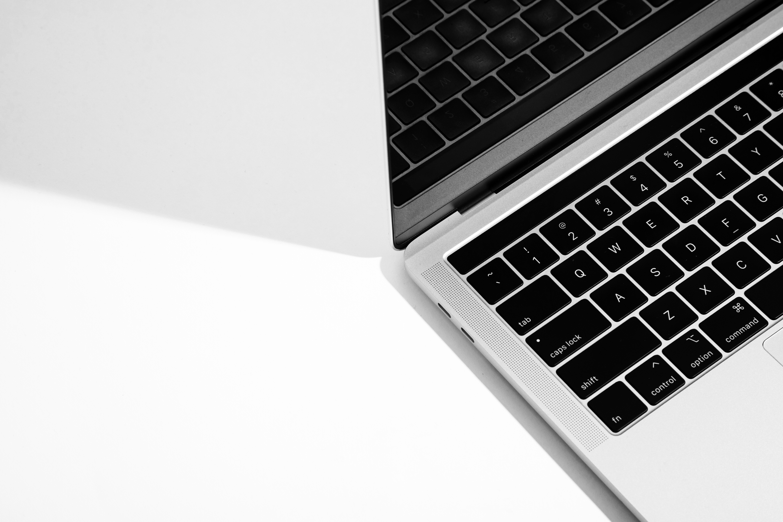 Close-up of a silver laptop keyboard with black keys, on a white surface.