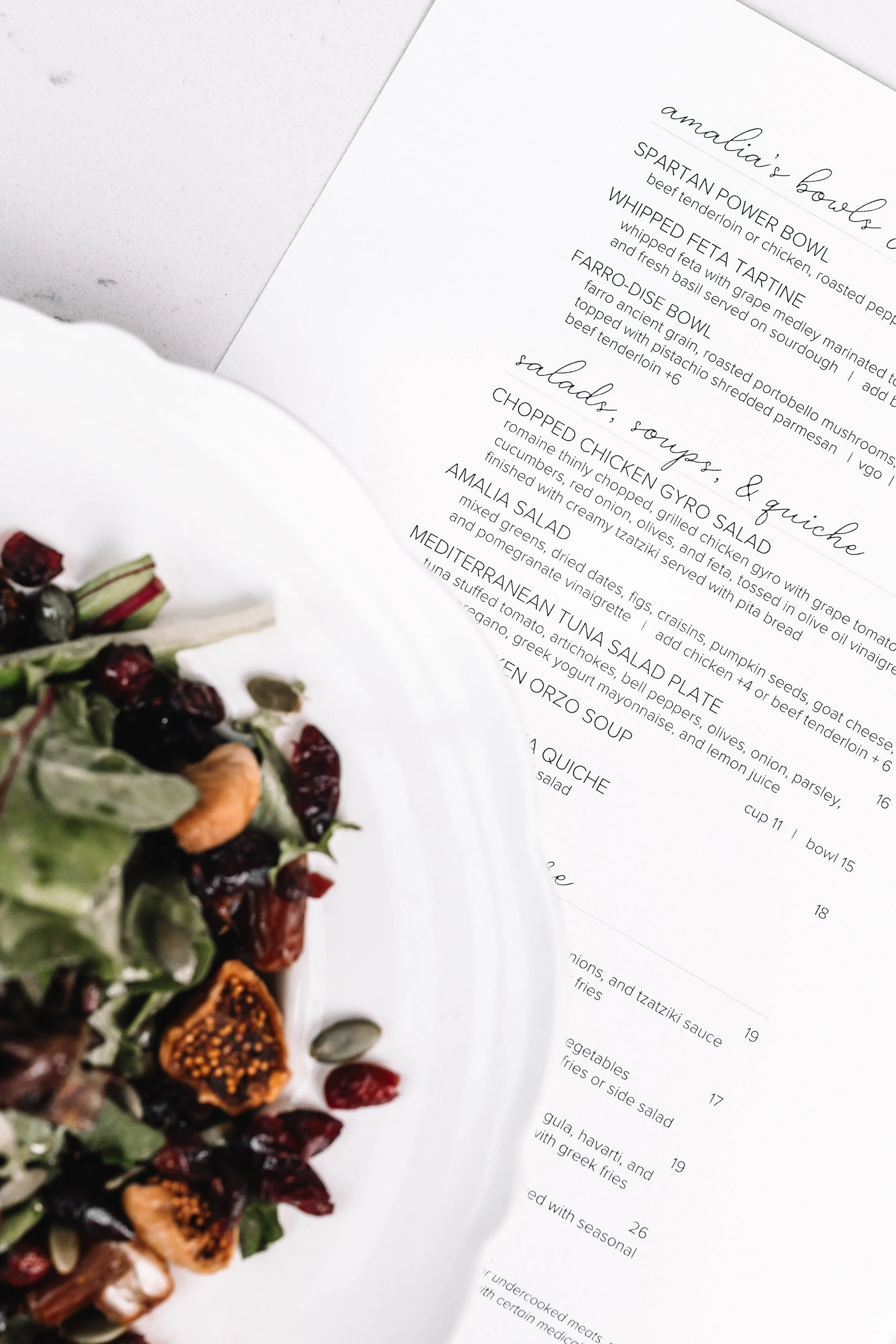 A white plate with a salad containing dried fruits, nuts, and seeds, partially visible in the foreground, next to a menu with printed text.