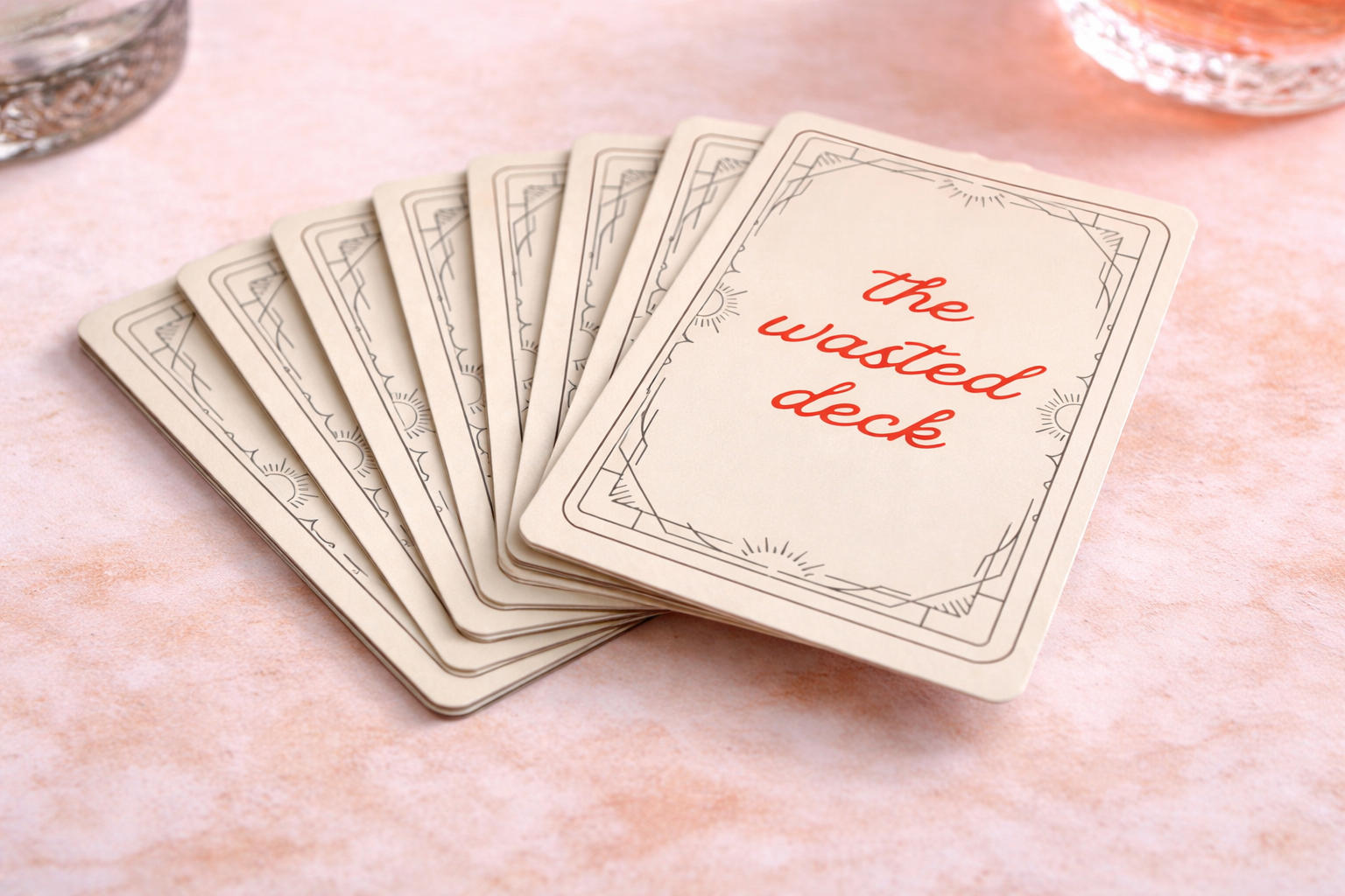 A deck of playing cards with the top card reading "the wasted deck" in red text on a light background, fanned out on a pink surface.
