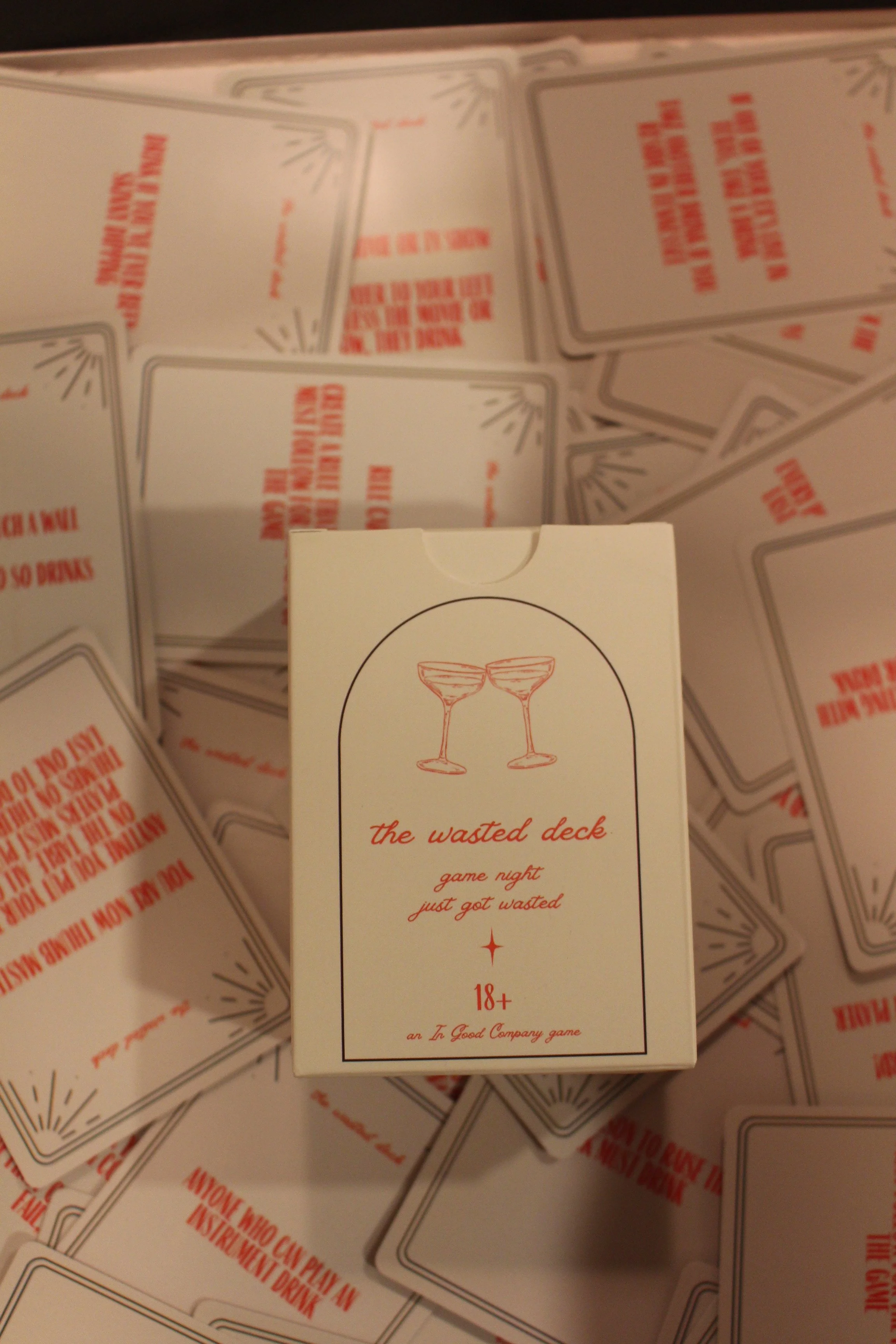 A deck of playing cards labeled "the wasted deck" with a slogan "game night just got wasted," featuring two crossed cocktail glasses on the box, surrounded by scattered similar decks.