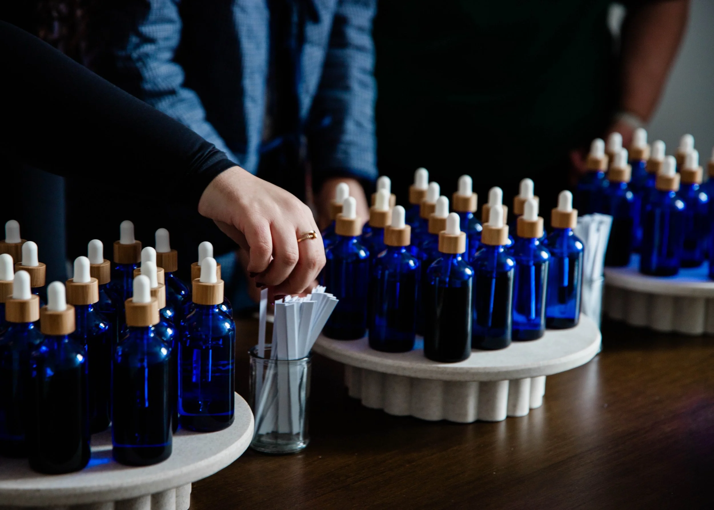 People organizing small blue bottles with brown and white dropper caps on wooden trays.