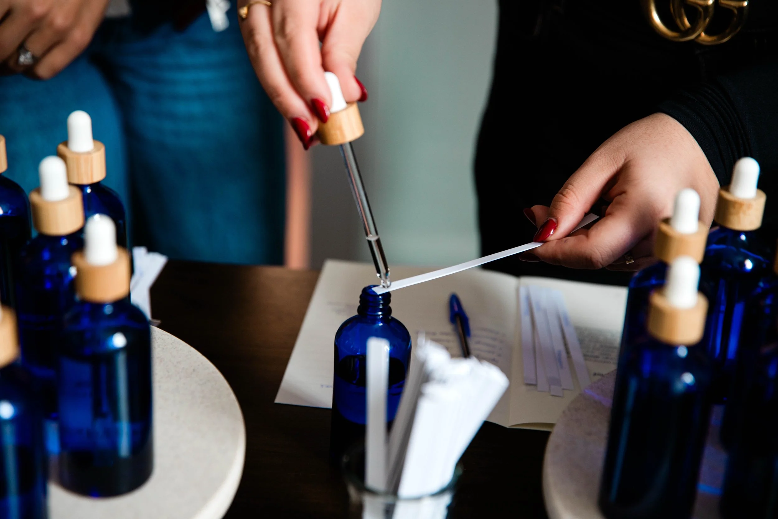 Someone using a dropper to transfer liquid from a blue glass bottle to a white strip on a table surrounded by similar bottles.