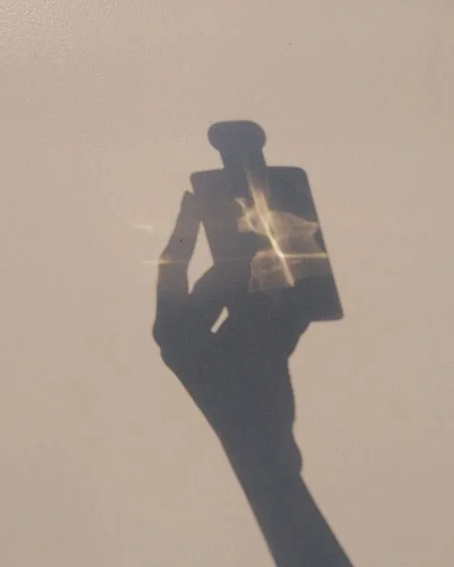 Shadow of a hand holding a perfume bottle.