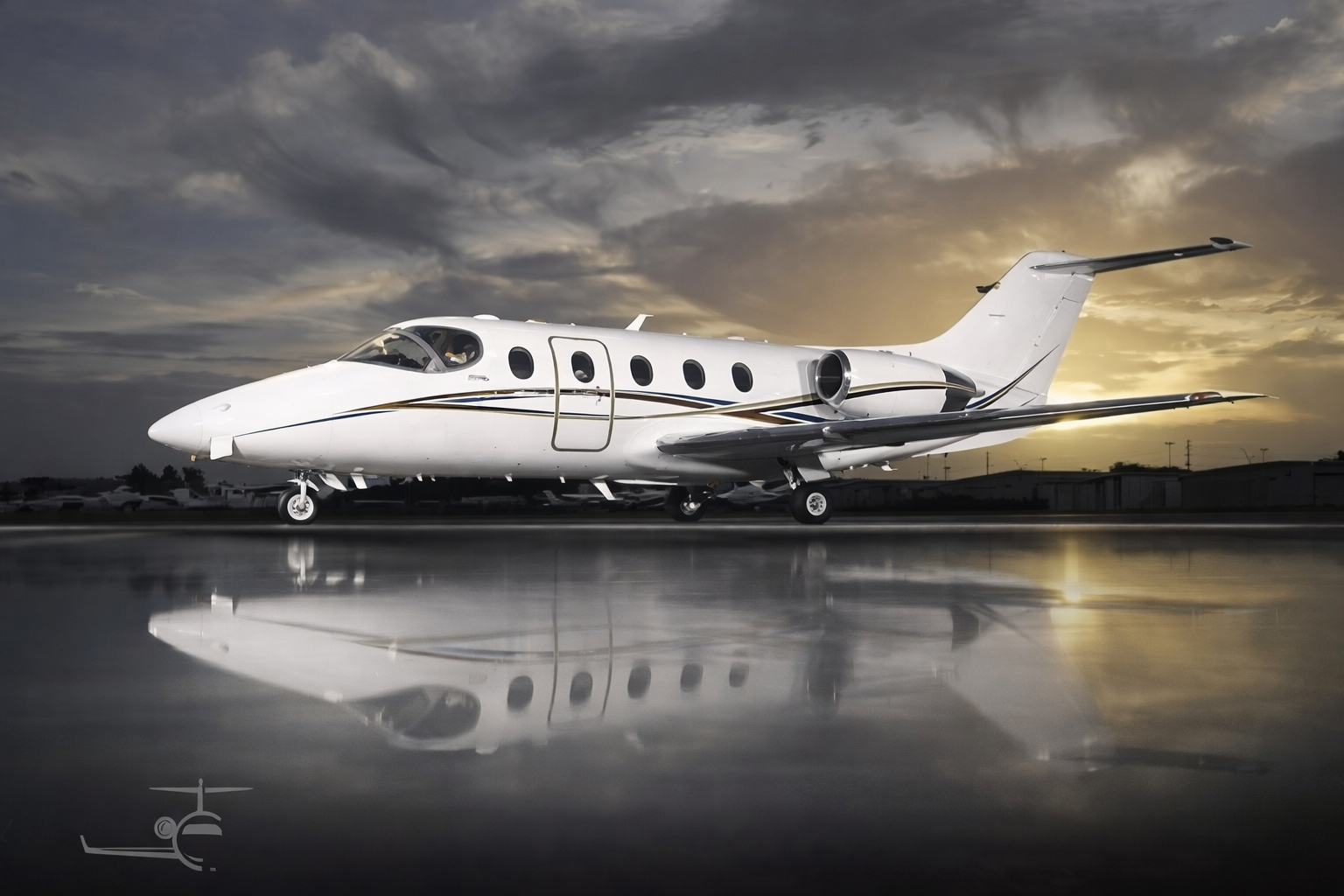 A sleek white private jet parked on the tarmac at sunset, with clouds in the sky and its reflection visible on the wet ground.