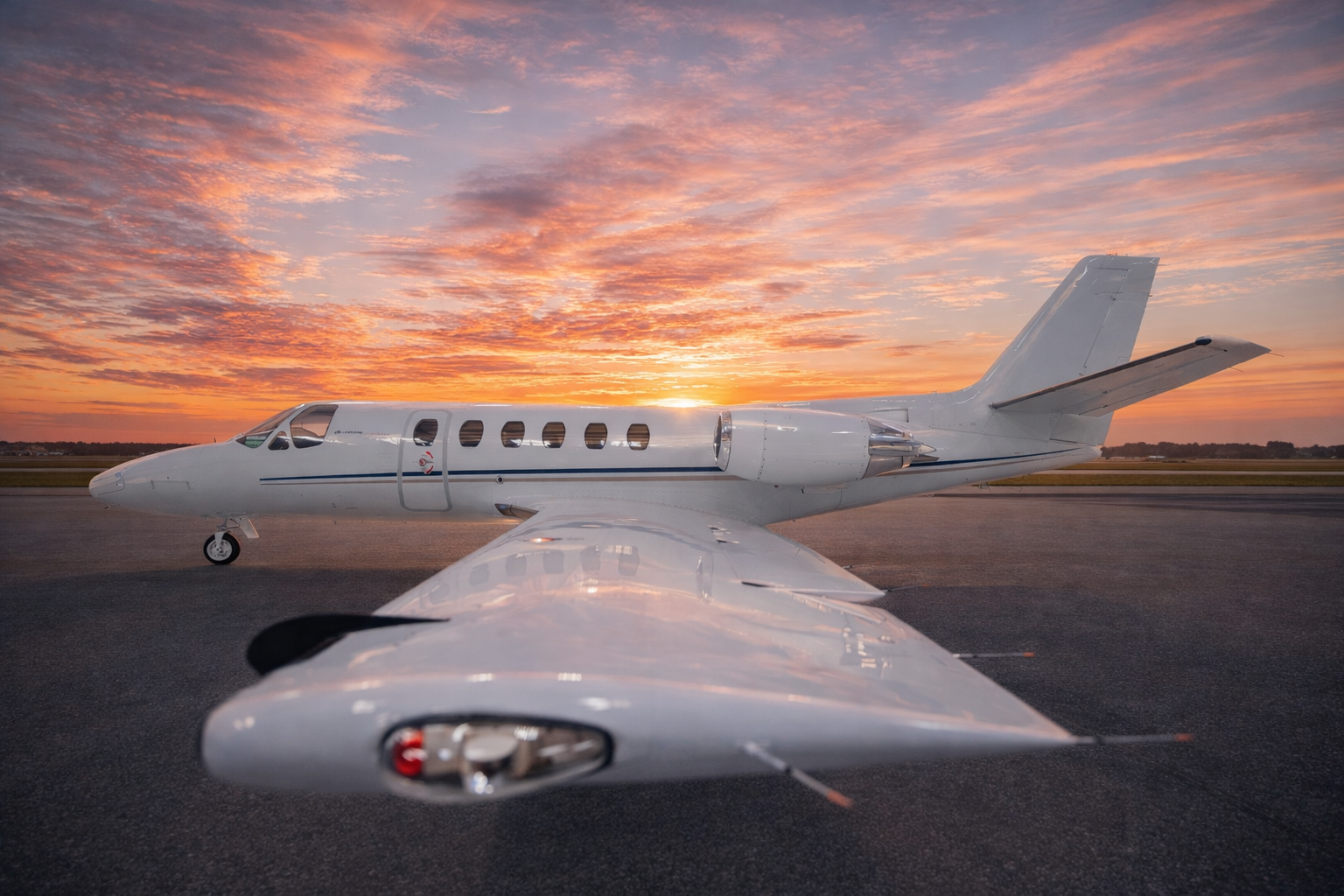 View of a private jet on the tarmac at sunset, with the sky filled with colorful clouds.