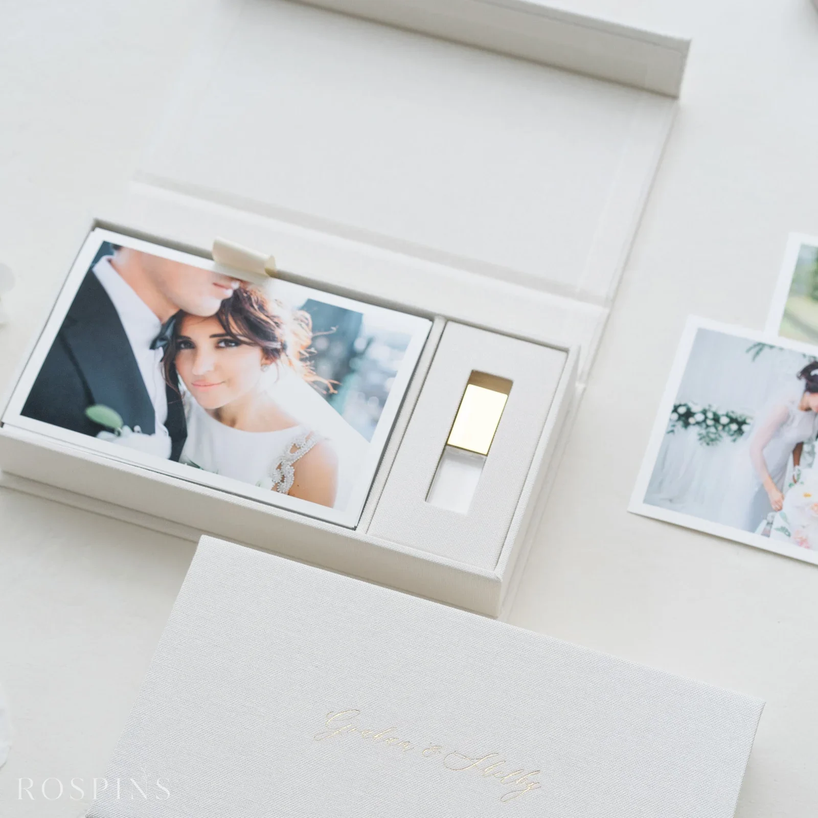 A set of wedding photographs, including a close-up of a bride and groom, in an elegant white box with a light switch next to it and a white wedding invitation with gold lettering.