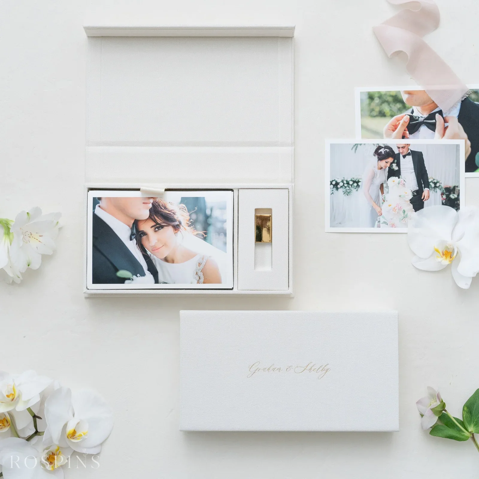 Wedding photos of a bride and groom, with flowers and a white card with elegant gold writing on a white surface.