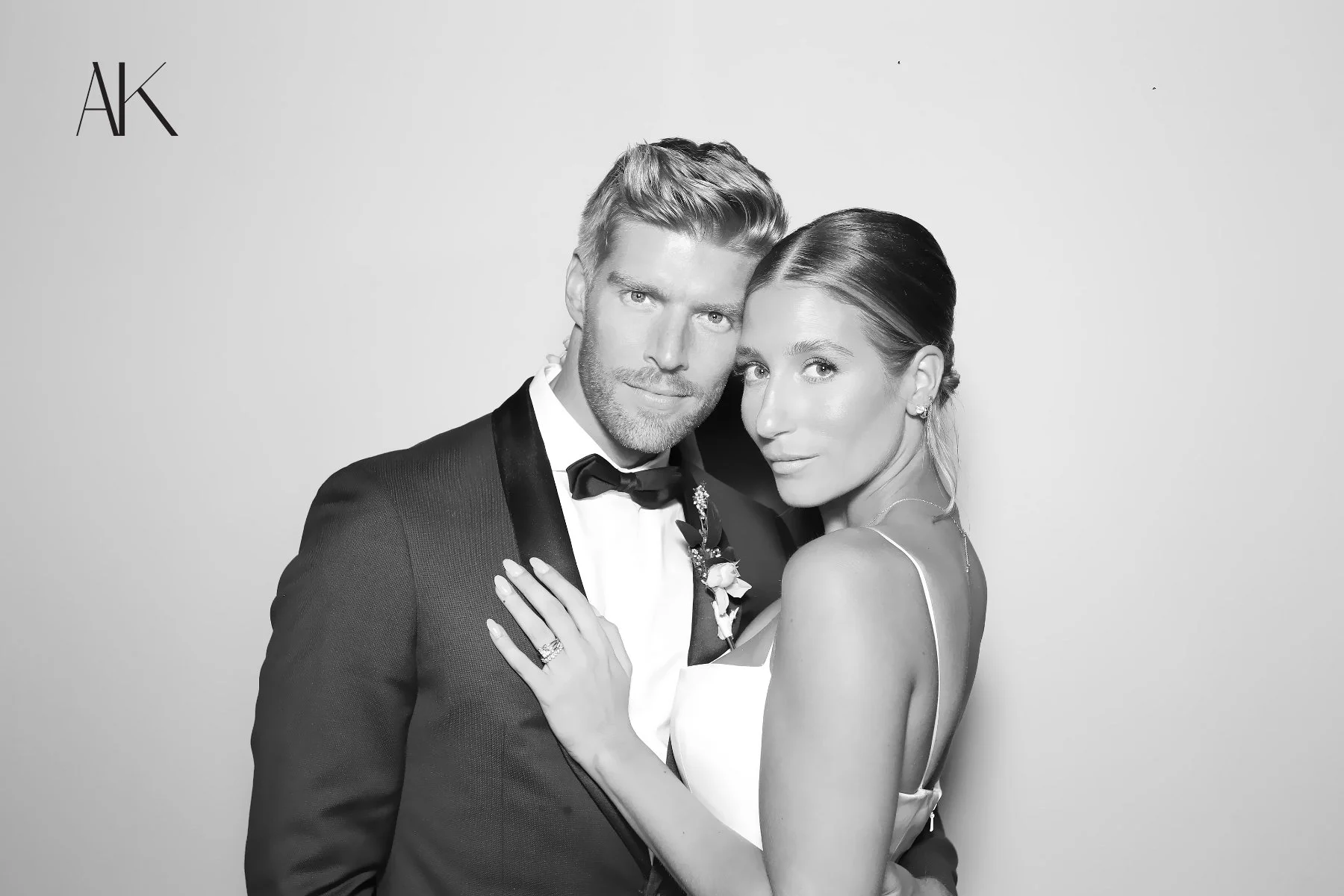 A black and white photo of a man and woman dressed in wedding attire, embracing each other and looking at the camera.