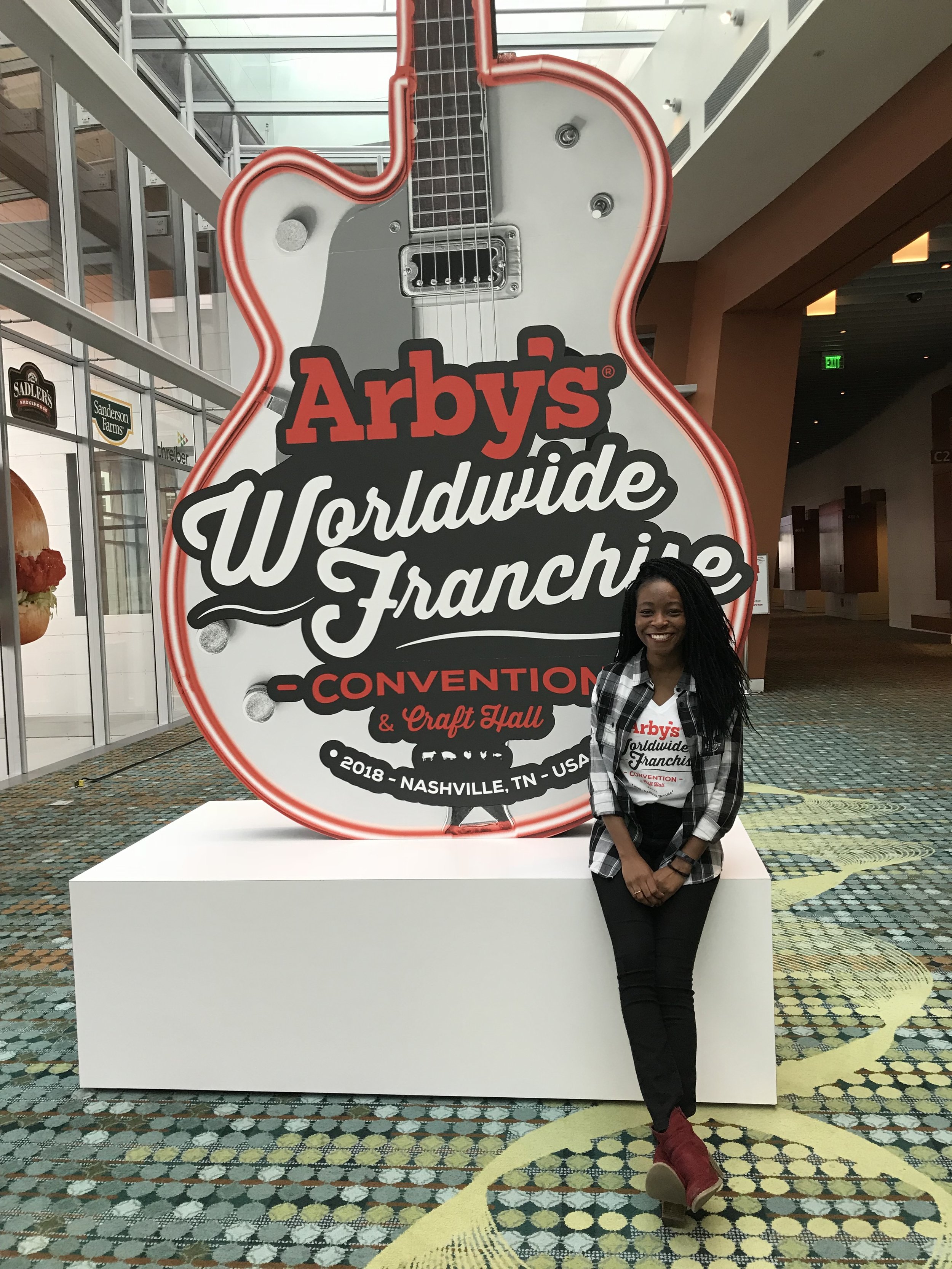 woman standing next to guitar statue with "Arby's Worldwide Franchise Convention" written on it