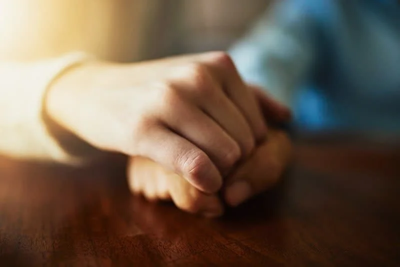 Two hands gently clasped on a wooden table, with soft lighting creating a warm ambiance.