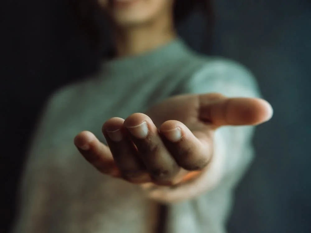 Close-up of a person extending their hand with palm up, fingers slightly curled, against a dark background.