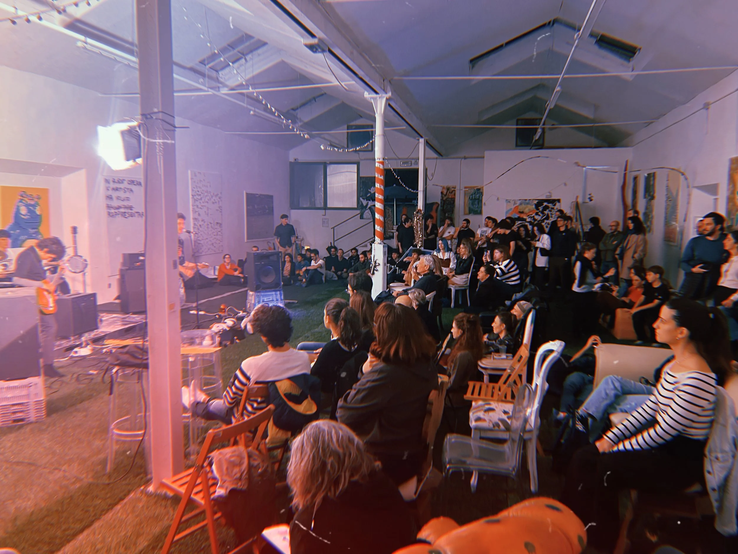 Un gruppo di persone sedute e in piedi all'interno di una sala durante uno spettacolo concerto a Lanarchico Prato, un capannone di 400 mq una volta sede di un lanificio, e ora lo studio d'artista più visitato d'Italia