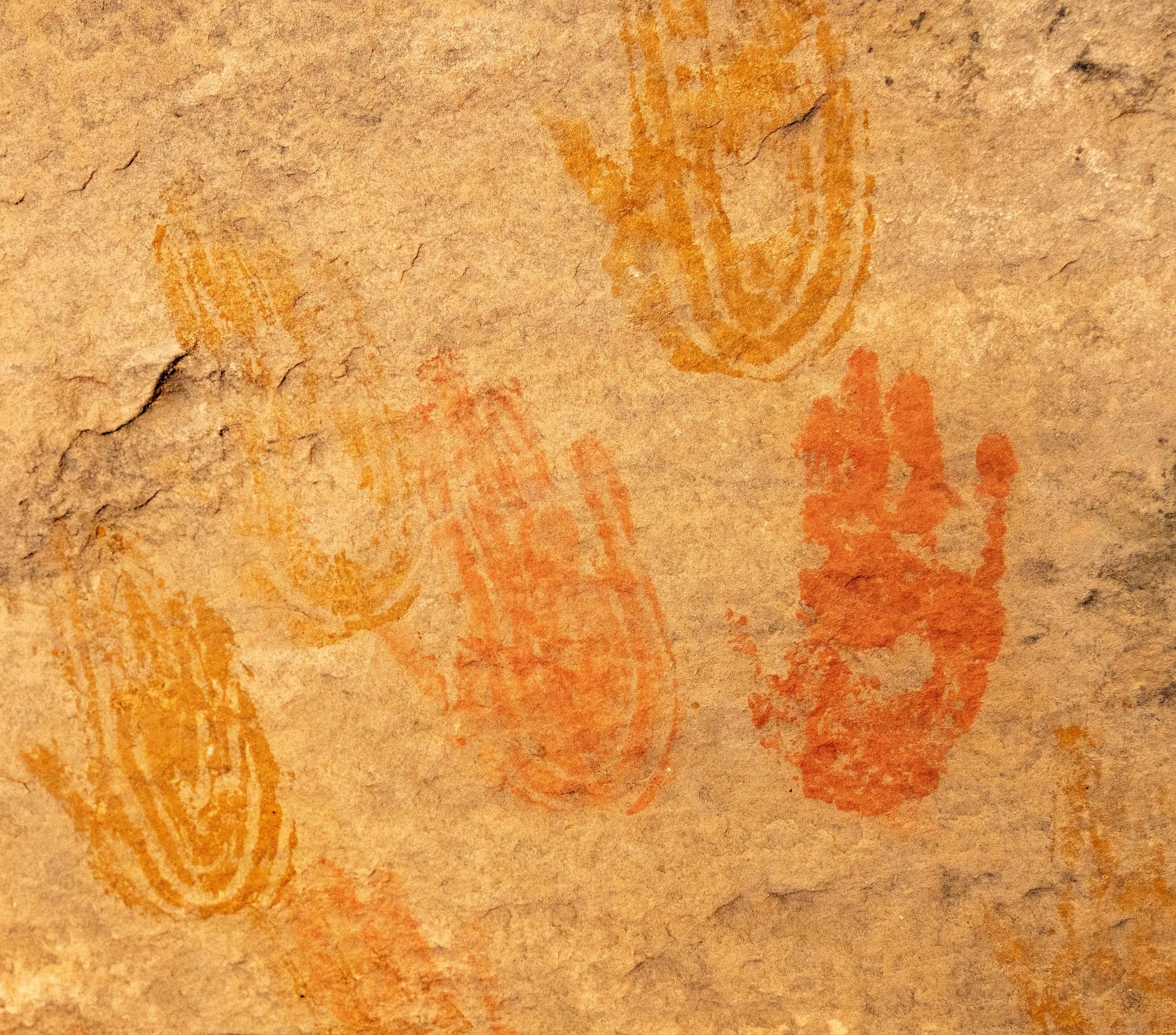 Multiple orange, red, and yellow handprints on a textured, tan paper background.